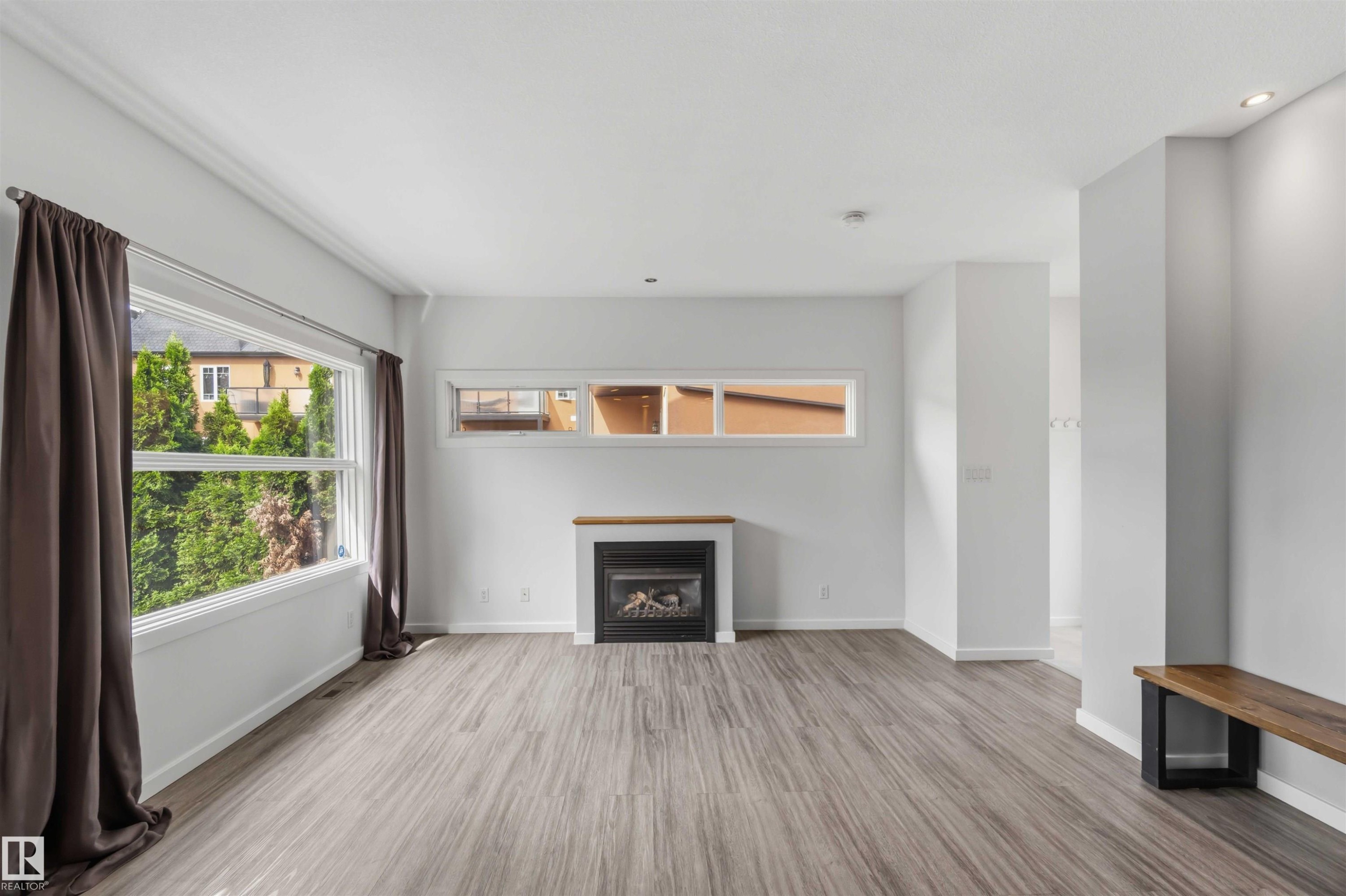 Spacious room featuring wood-finish flooring, white walls, and a gas fireplace with a wood mantle - #1 14315 Stony Plain Nw, Edmonton, AB - Indoor Photo Showing Living Room With Fireplace