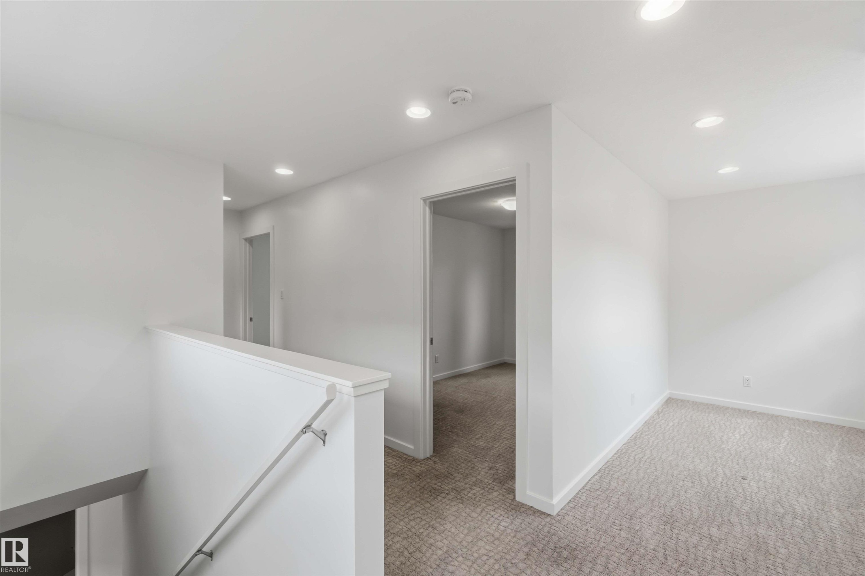 Upper-level landing featuring a white painted railing, recessed lighting, and light-toned patterned carpeting - #1 14315 Stony Plain Nw, Edmonton, AB - Indoor Photo Showing Other Room