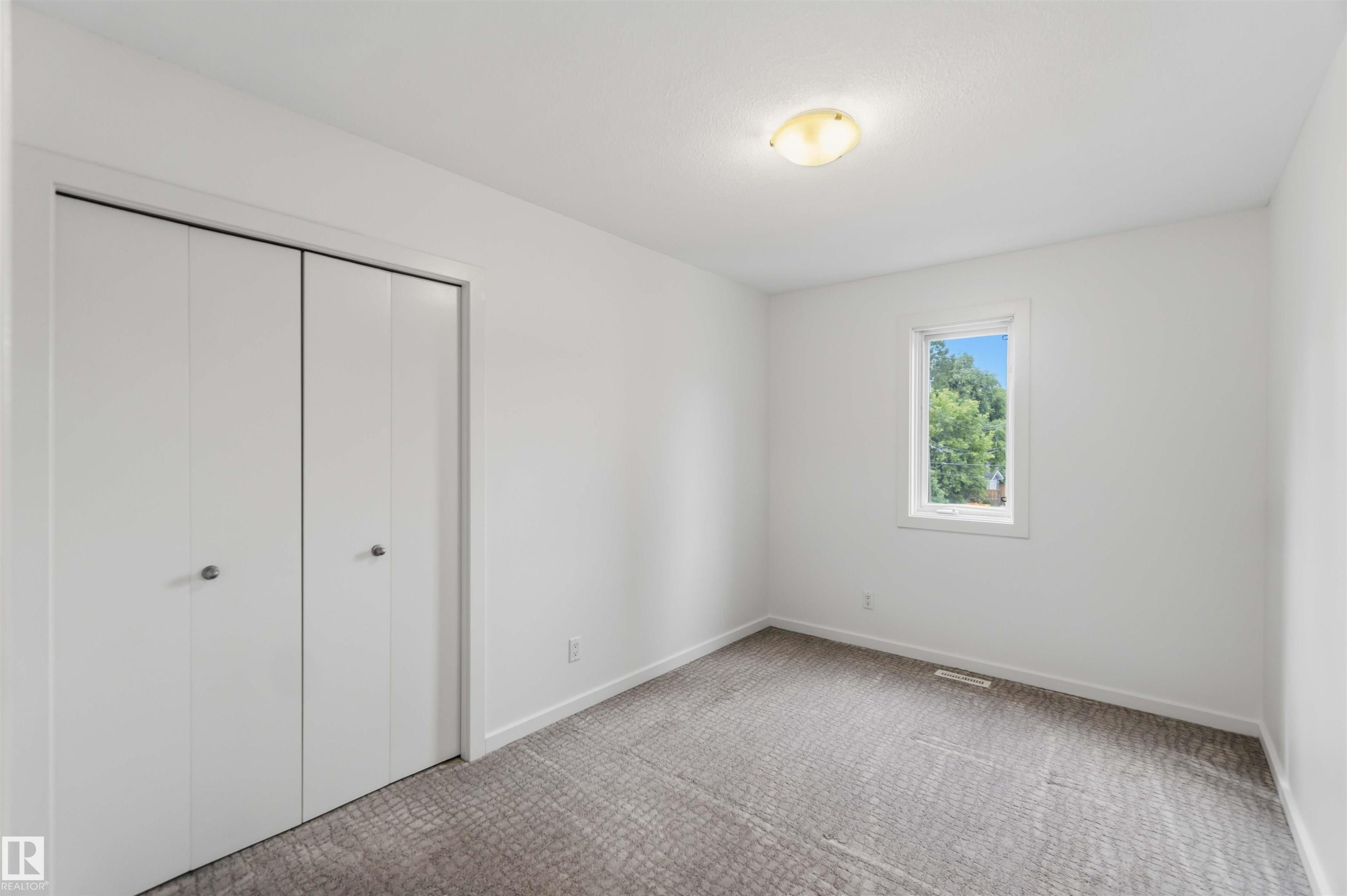 Spacious room featuring white walls, gray patterned carpet, a single window, white bi-fold closet doors, and a flush-mount ceiling light fixture - #1 14315 Stony Plain Nw, Edmonton, AB - Indoor Photo Showing Other Room