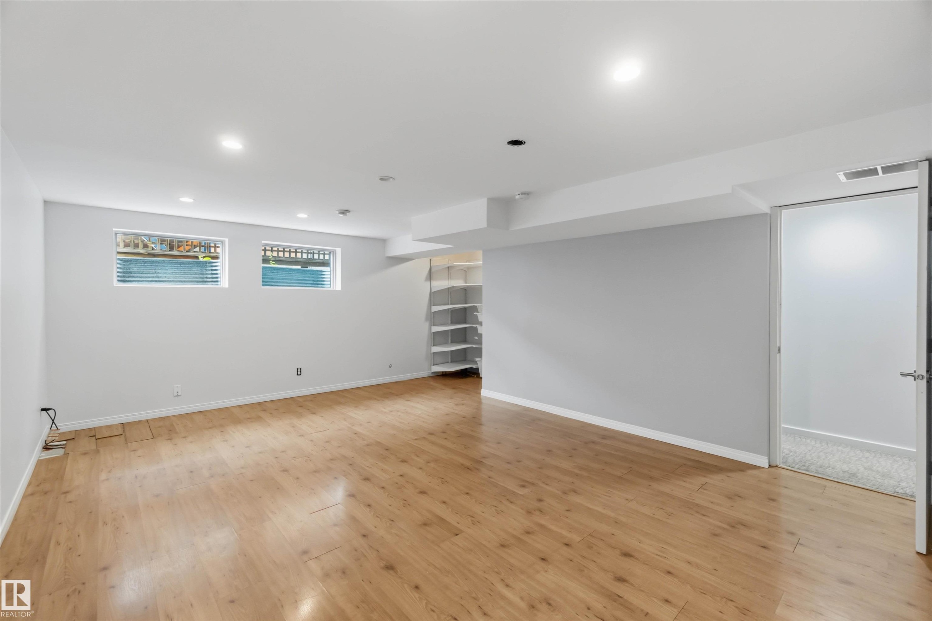 Spacious room featuring wood-finish flooring, recessed lighting, and crisp white walls - #1 14315 Stony Plain Nw, Edmonton, AB - Indoor