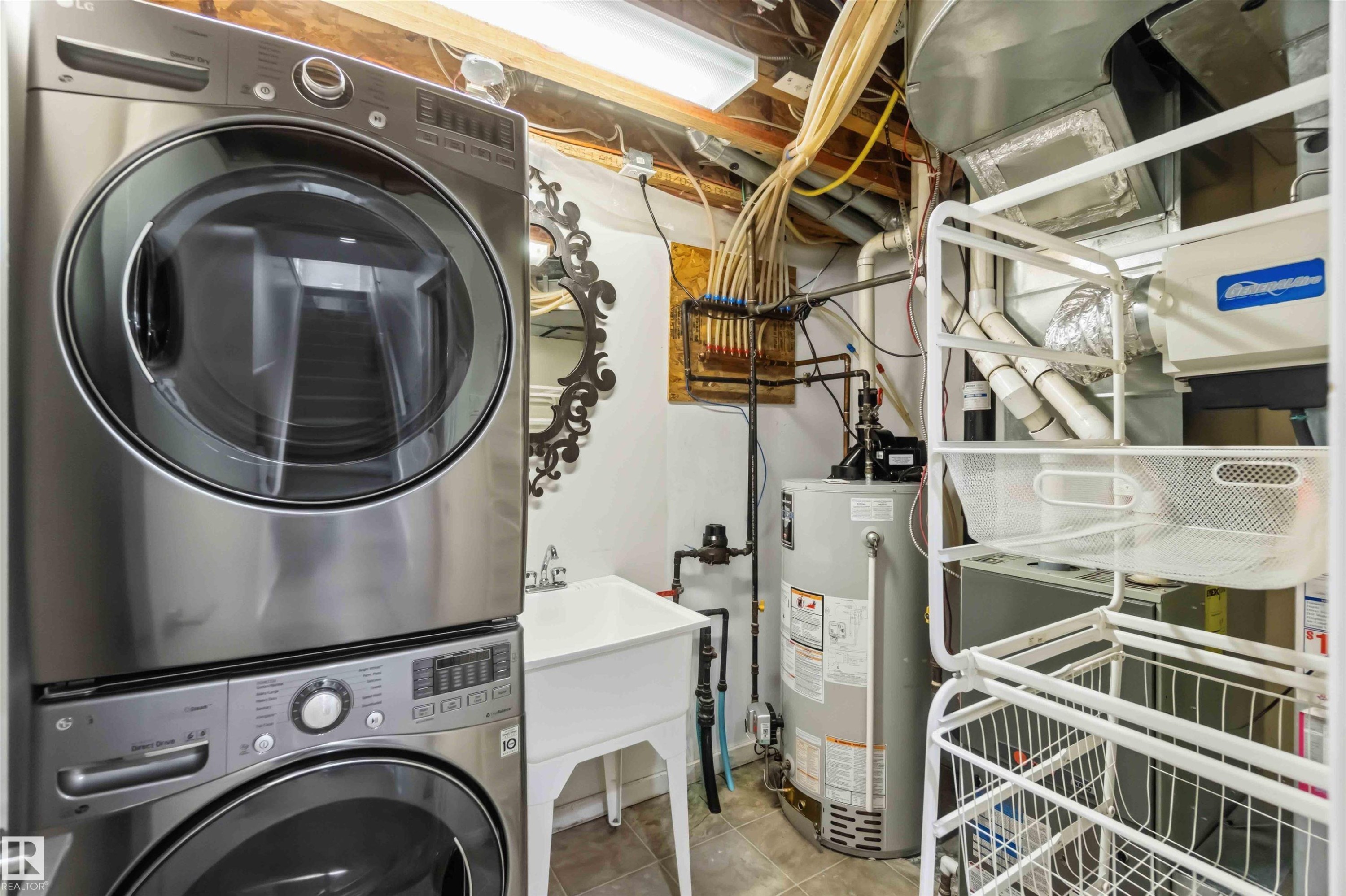 Stackable stainless steel washer and dryer unit, utility sink, and water heater - #1 14315 Stony Plain Nw, Edmonton, AB - Indoor Photo Showing Laundry Room