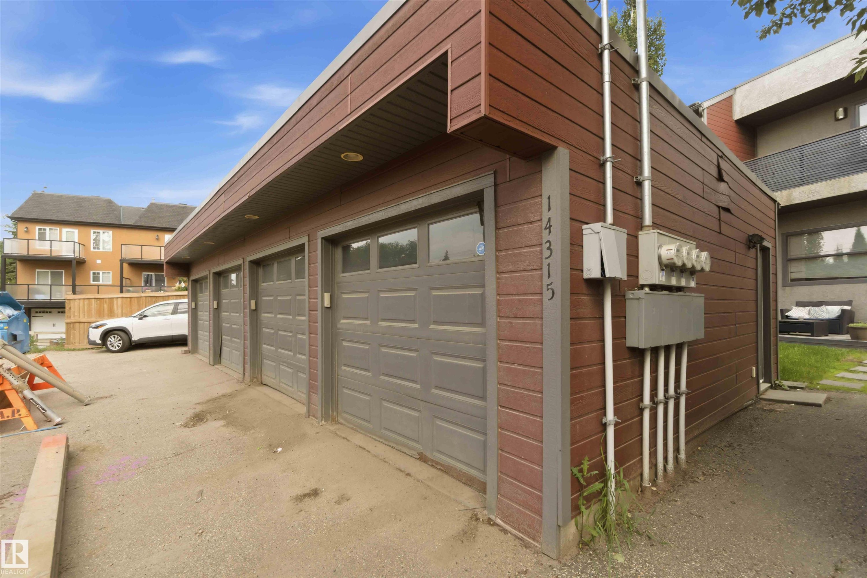 Exterior featuring horizontal brown siding, multiple garage doors with window inserts, individual utility meters, and an integrated address number - #1 14315 Stony Plain Nw, Edmonton, AB - Outdoor With Exterior