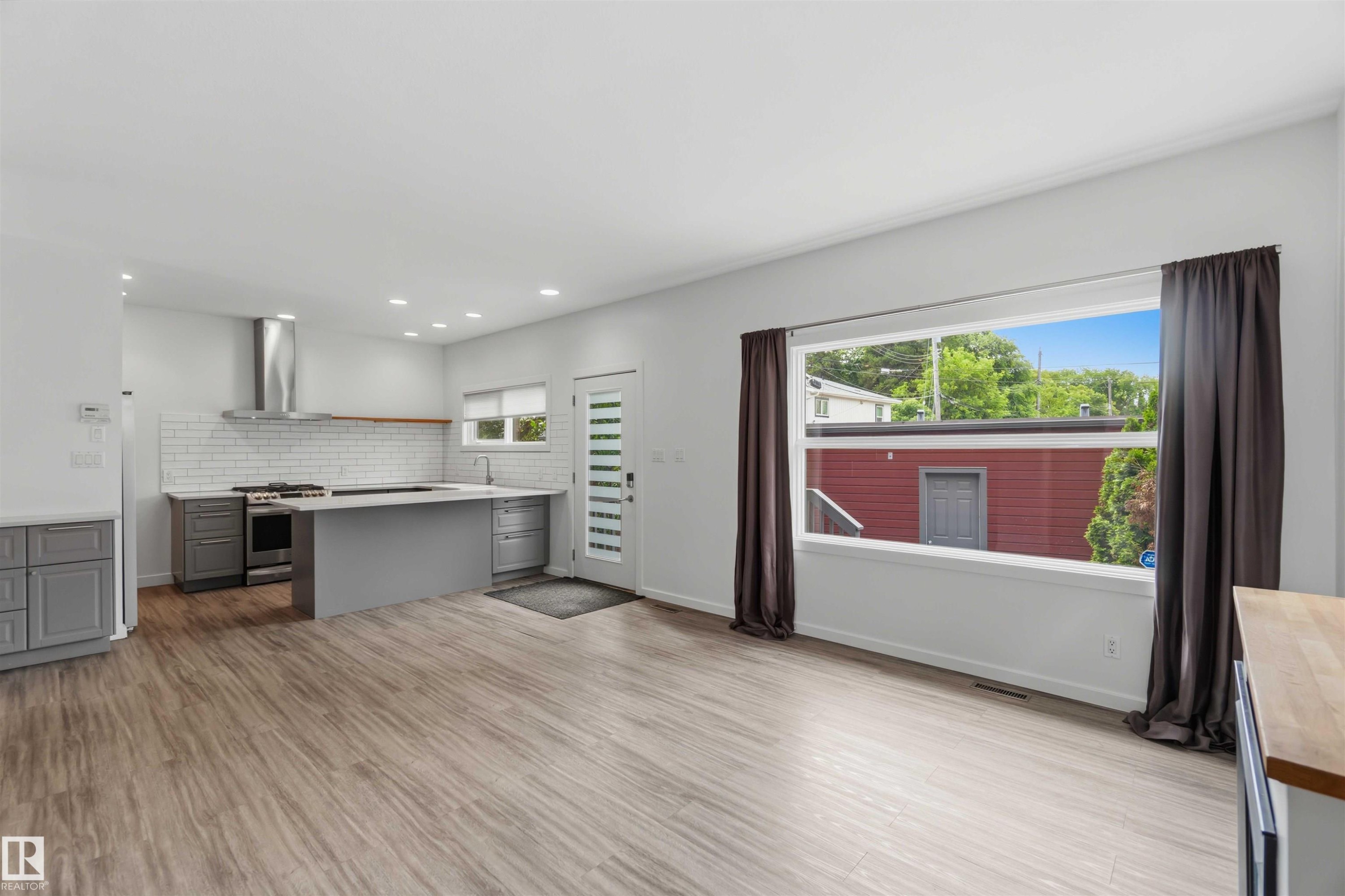 Open concept living area with wood-finish flooring, recessed lighting, and a wide window with dark drapery - #1 14315 Stony Plain Nw, Edmonton, AB - Indoor Photo Showing Kitchen