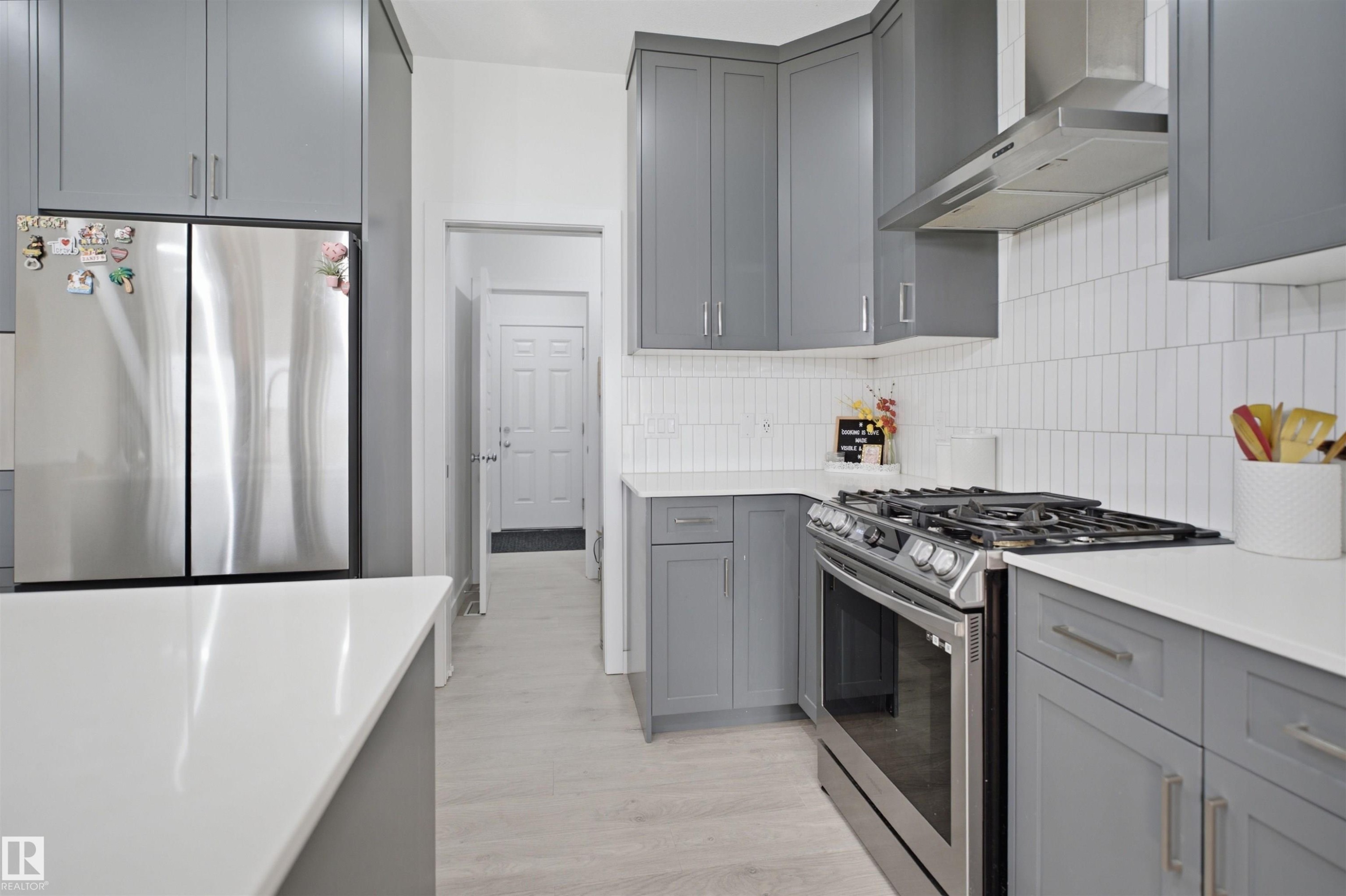 Contemporary kitchen featuring grey cabinetry, white countertops, stainless steel appliances, a gas range with matching hood, and vertical subway tile backsplash - 2508 193 Street Nw, Edmonton, AB - Indoor Photo Showing Kitchen With Stainless Steel Kitchen With Upgraded Kitchen