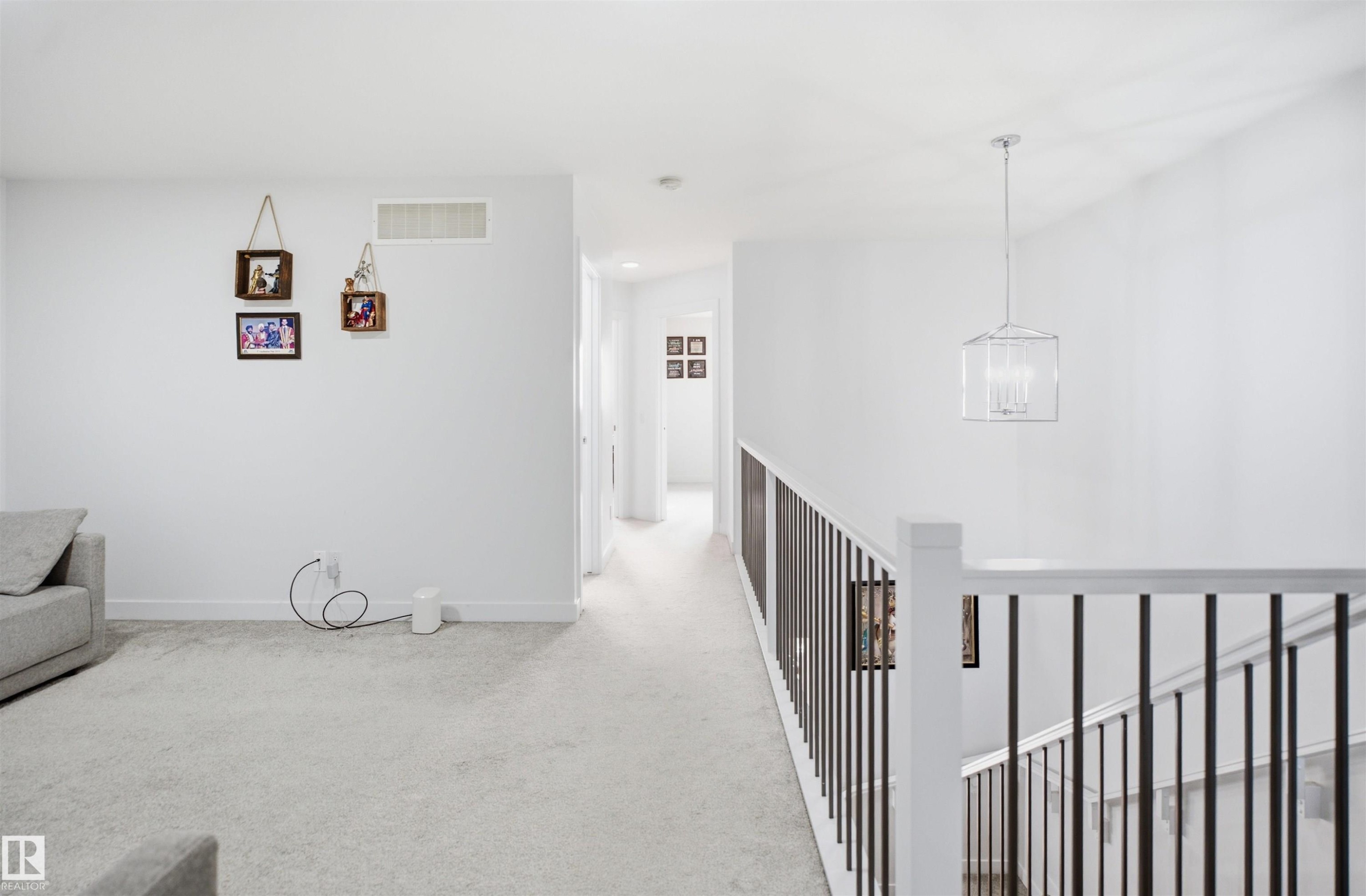 Upper-level landing featuring light-toned carpet flooring, white walls, and a contemporary chandelier - 2508 193 Street Nw, Edmonton, AB - Indoor