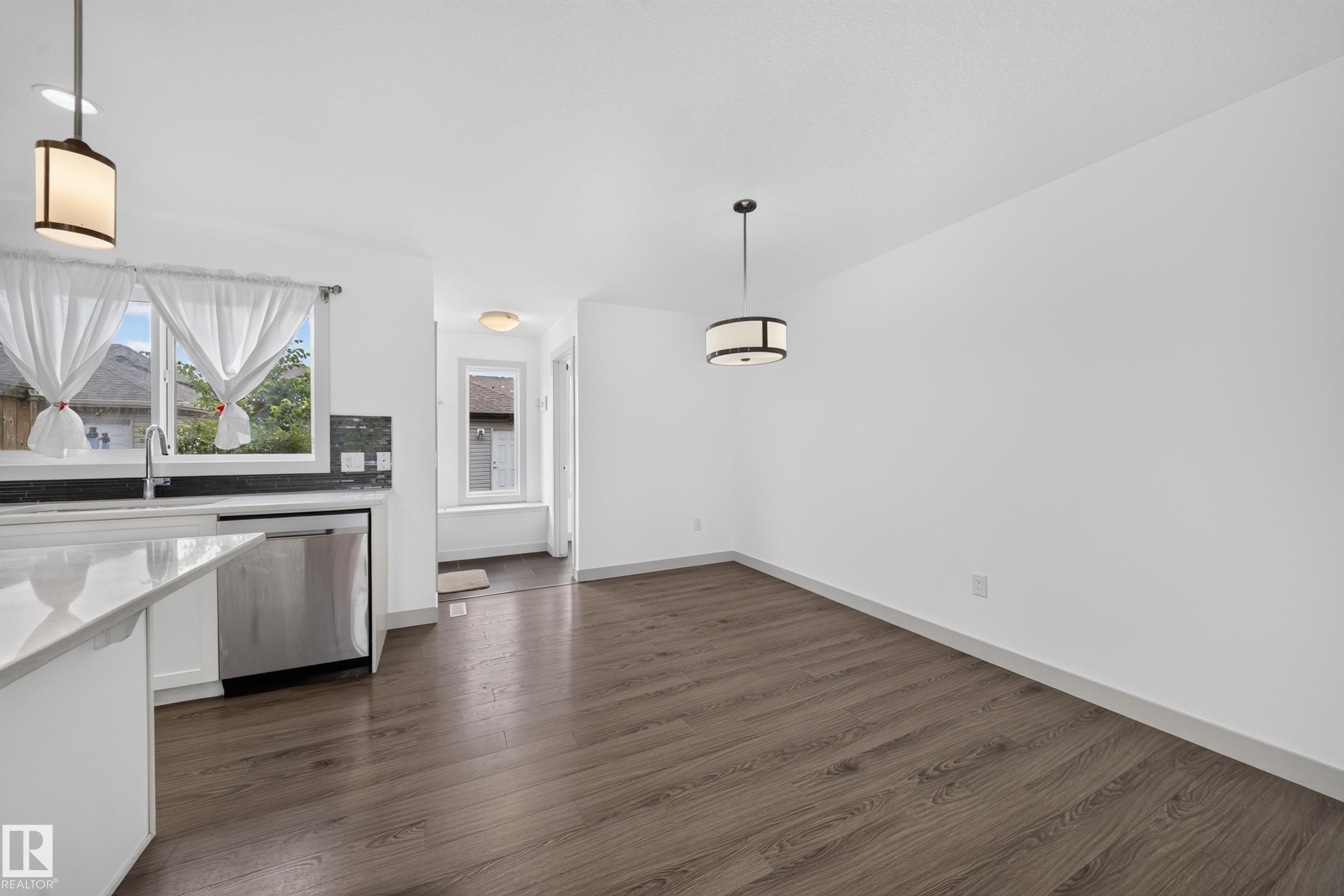 Open-concept space featuring wood-finish flooring, white walls, and contemporary pendant lighting - 227 Cy Becker Blvd, Edmonton, AB
