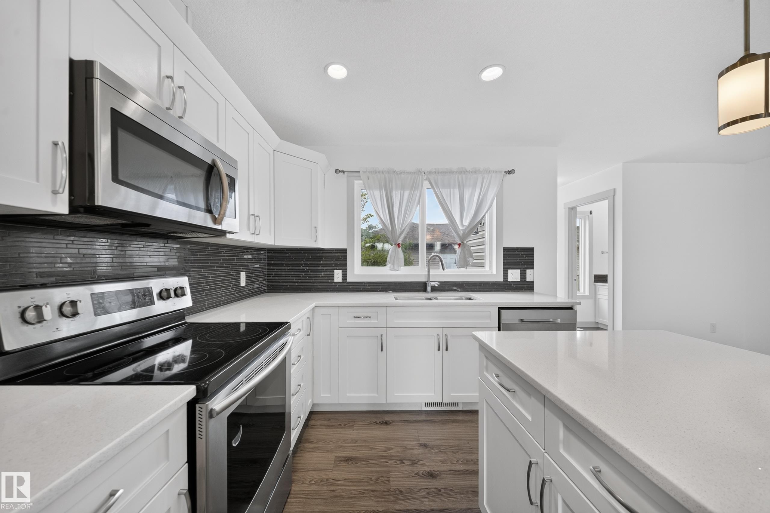 Modern kitchen featuring white cabinetry, stainless steel appliances, dark tile backsplash, a center island, and wood-finish flooring - 227 Cy Becker Blvd, Edmonton, AB