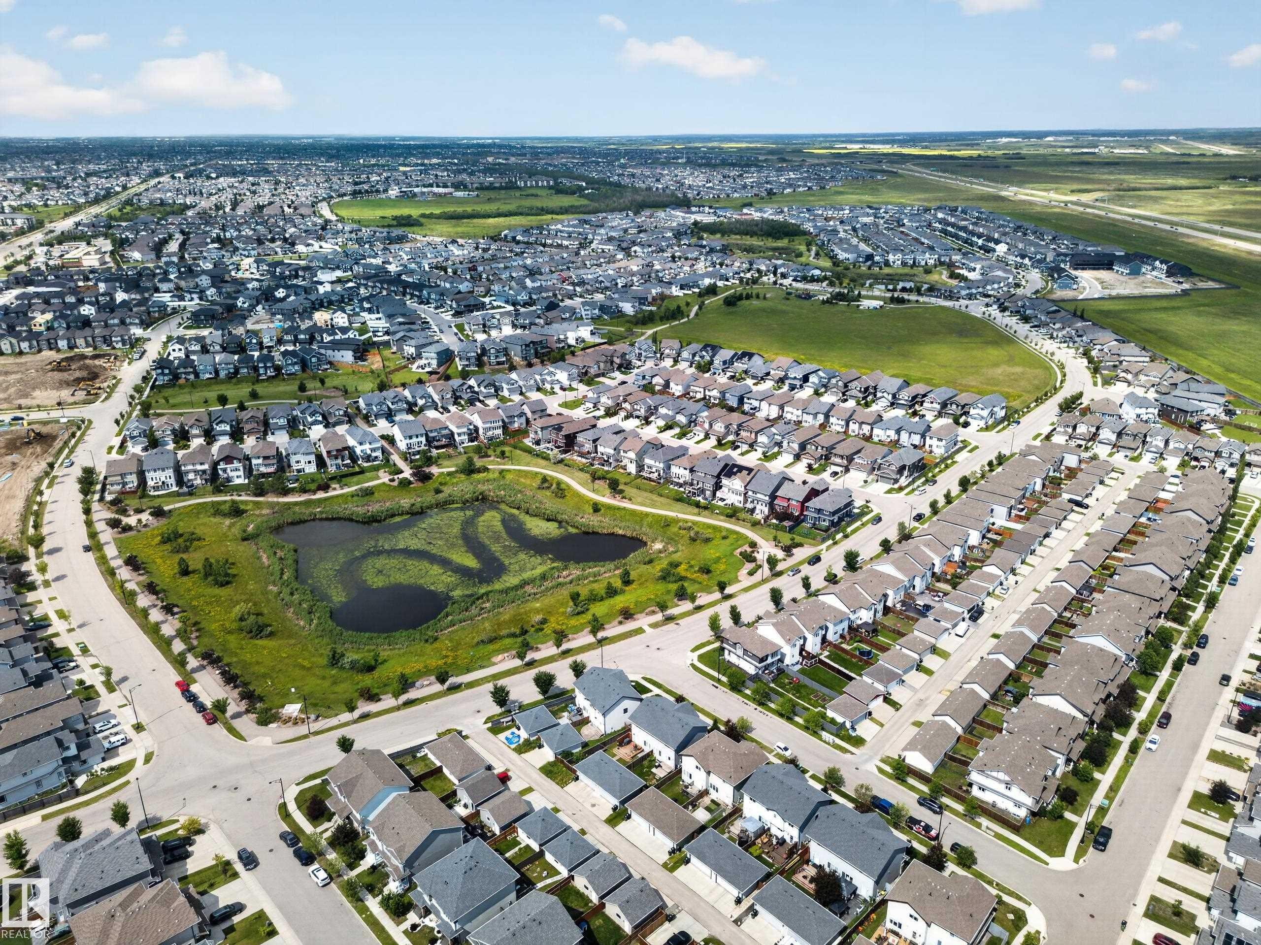 Expansive aerial capturing a suburban development featuring a central wetland area with walking paths - 227 Cy Becker Blvd, Edmonton, AB