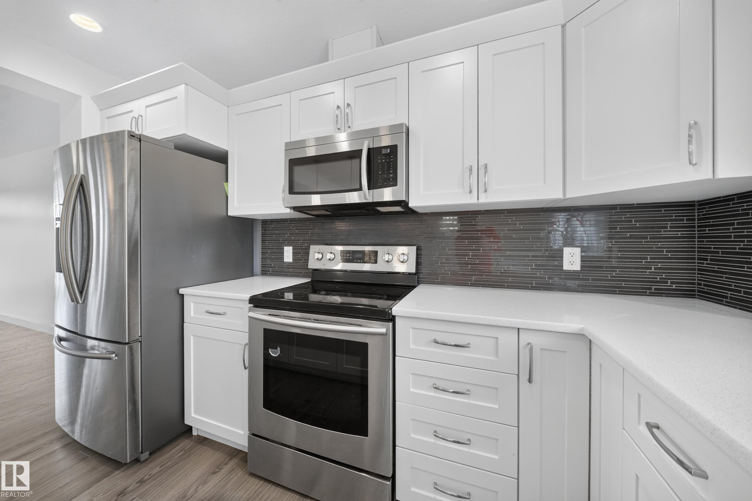 Contemporary kitchen featuring white cabinetry, stainless steel appliances, light countertops, and a dark mosaic tile backsplash - 227 Cy Becker Blvd, Edmonton, AB
