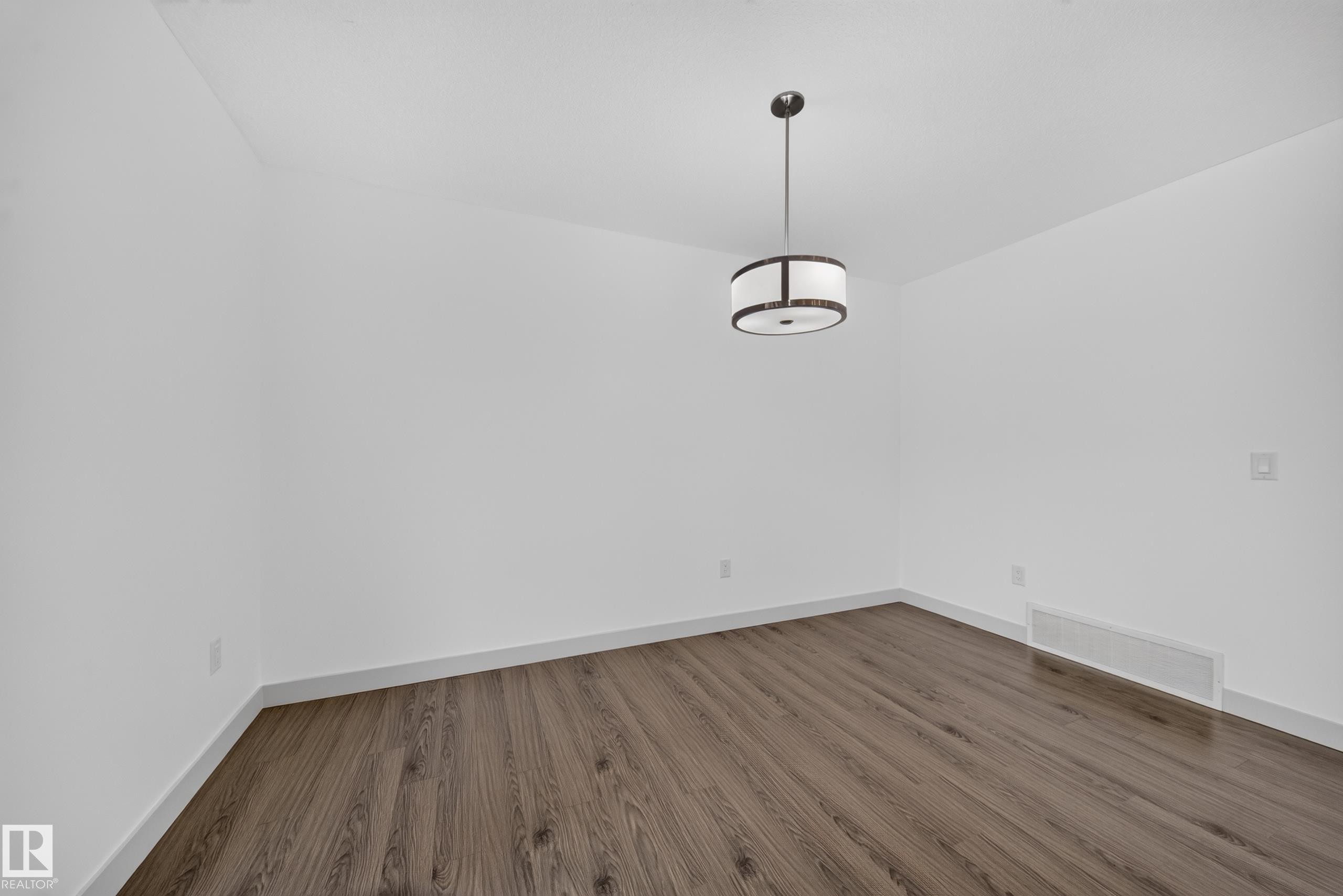 Spacious room featuring wood-finish flooring and a contemporary drum pendant light fixture - 227 Cy Becker Blvd, Edmonton, AB