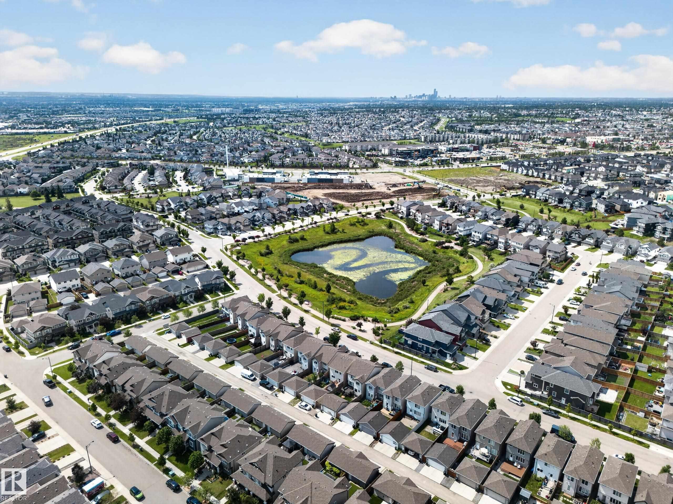 Aerial perspective of a developed residential community featuring an artificial pond surrounded by green spaces - 227 Cy Becker Blvd, Edmonton, AB