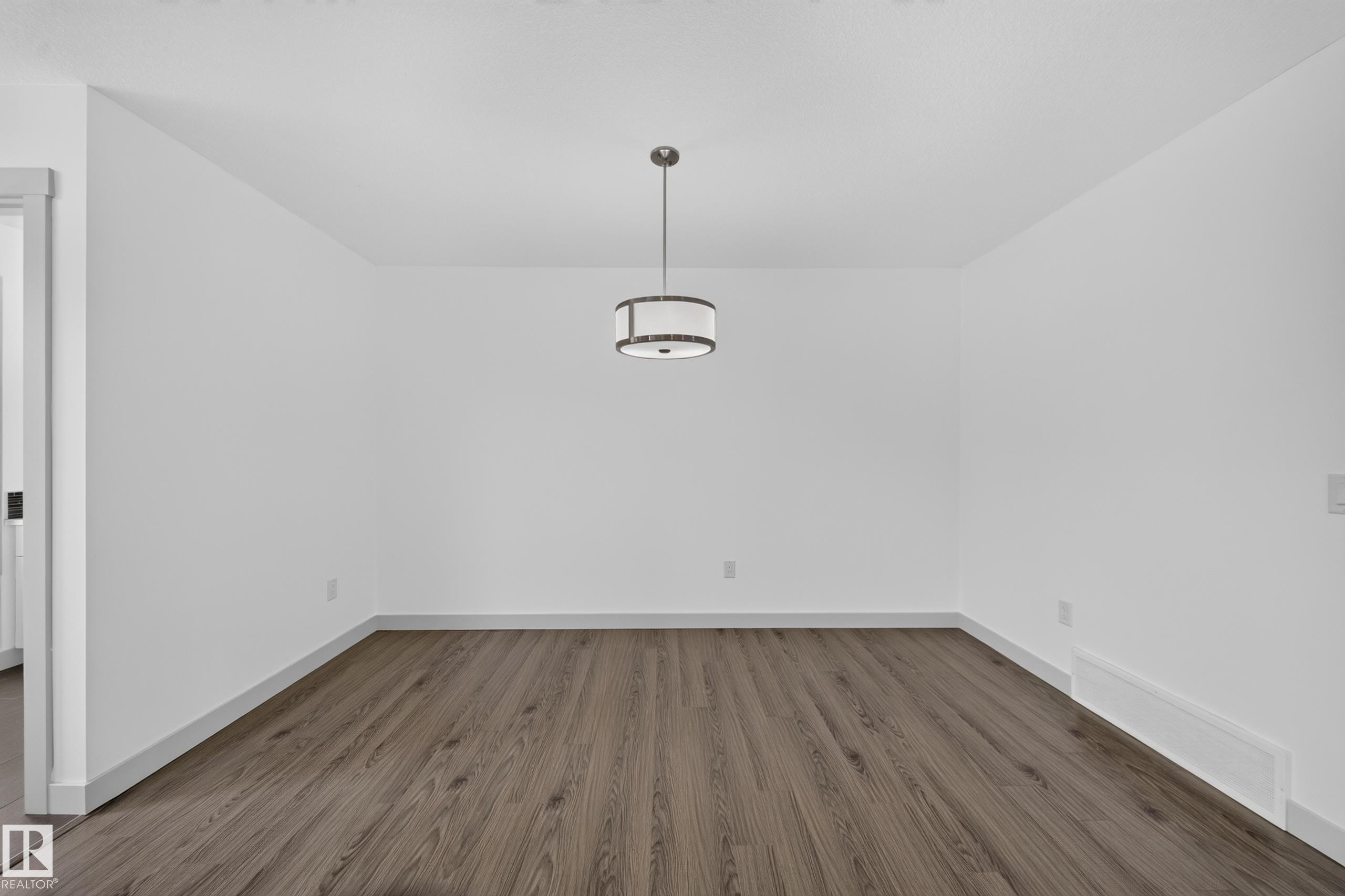 Spacious room with wood-finish flooring and a contemporary drum pendant light fixture - 227 Cy Becker Blvd, Edmonton, AB