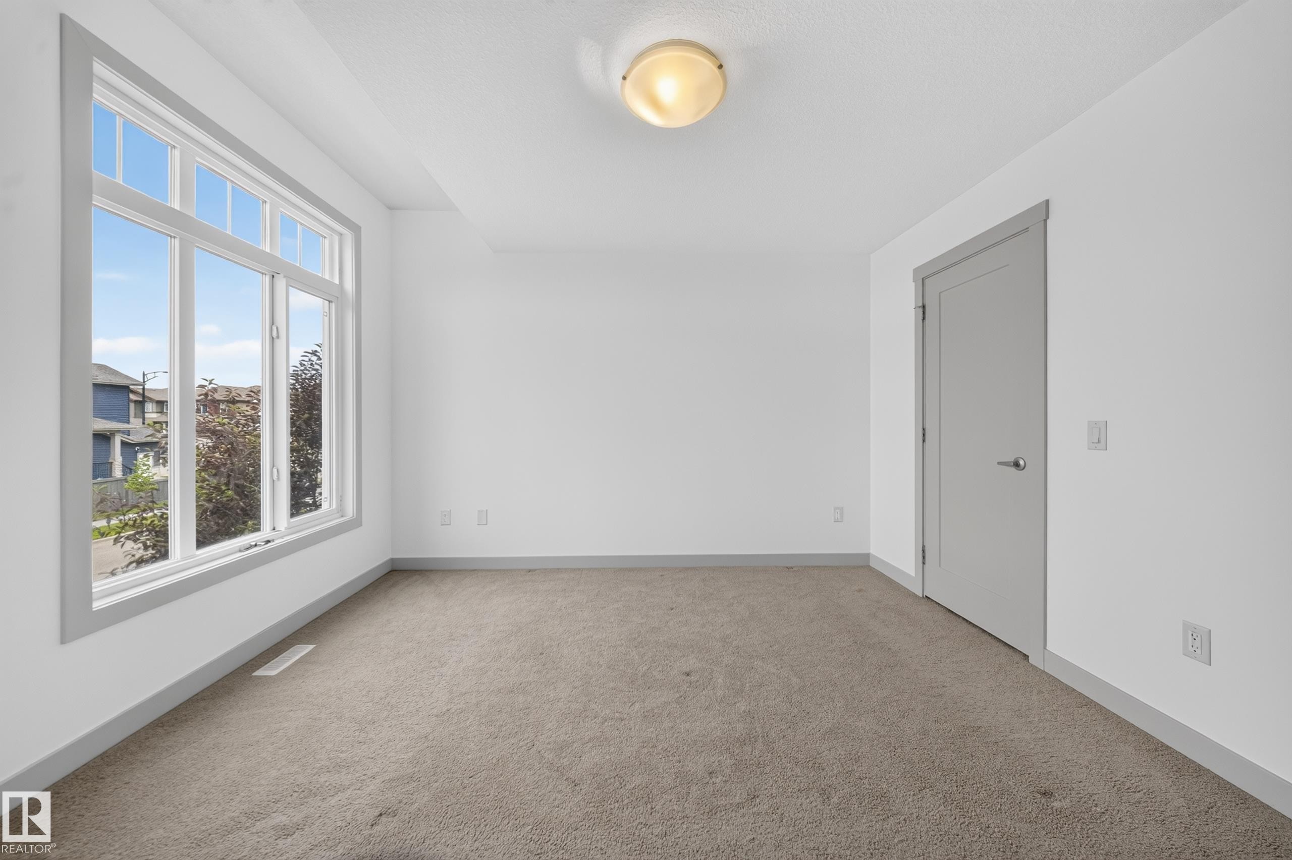 Room featuring a large multi-pane window, neutral-toned carpeting, white walls, and a flush mount ceiling light - 227 Cy Becker Blvd, Edmonton, AB