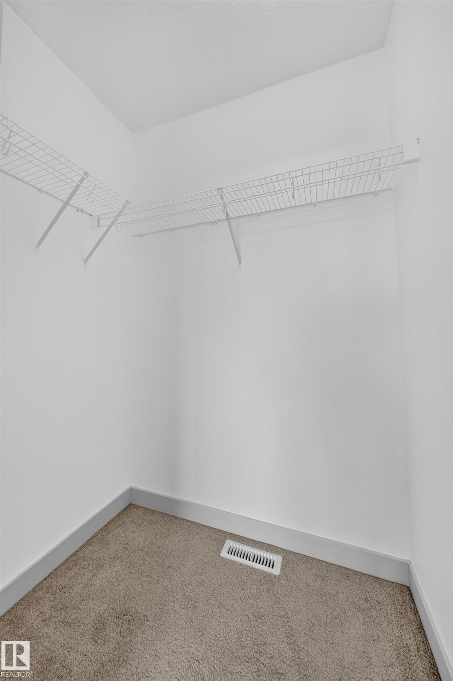 Walk-in closet featuring built-in wire shelving, plush carpeting, white baseboards, and a floor vent - 227 Cy Becker Blvd, Edmonton, AB