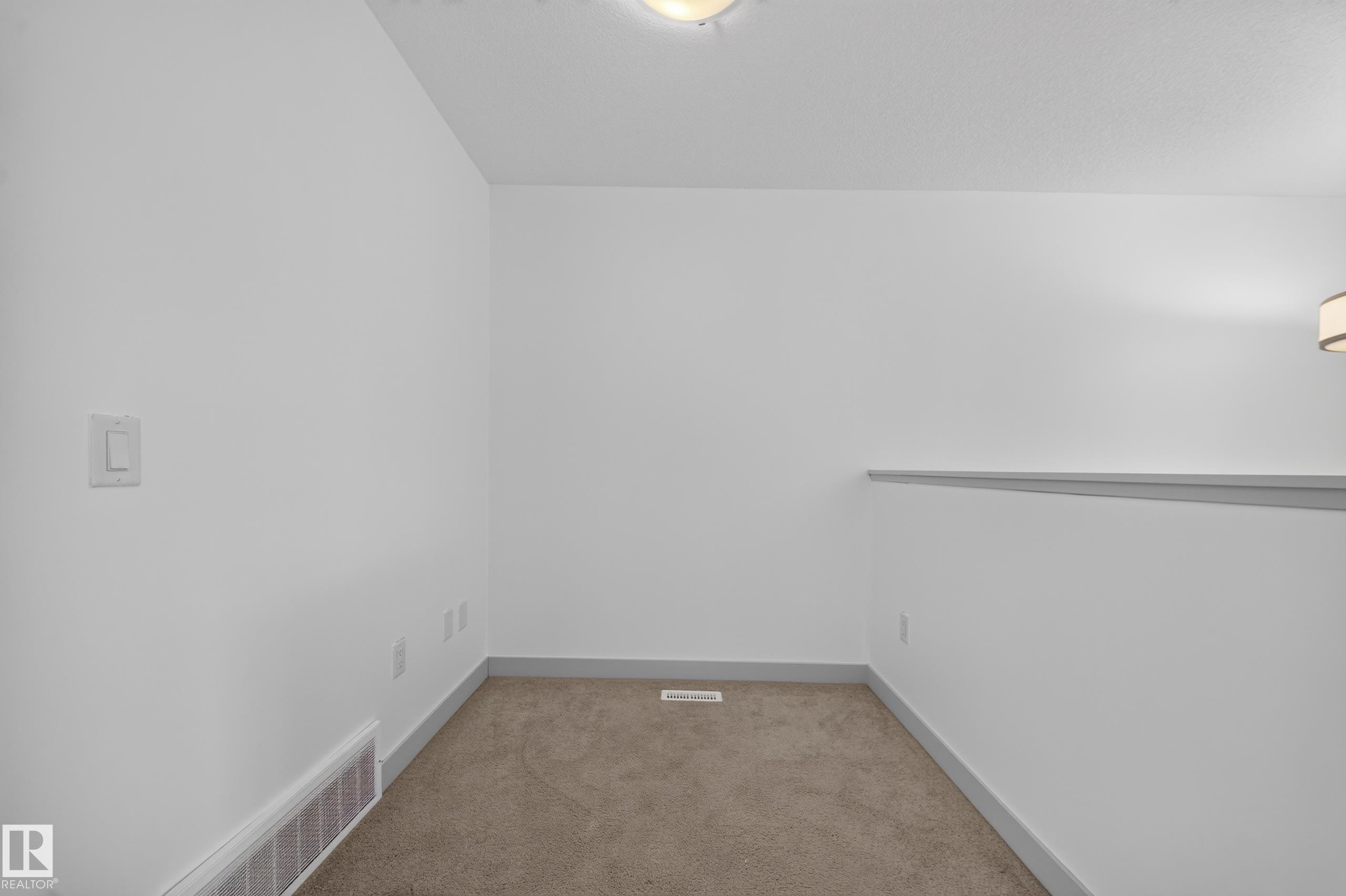 Carpeted room featuring white walls, gray baseboards, a ceiling-mounted light fixture, and a wall-mounted light fixture - 227 Cy Becker Blvd, Edmonton, AB
