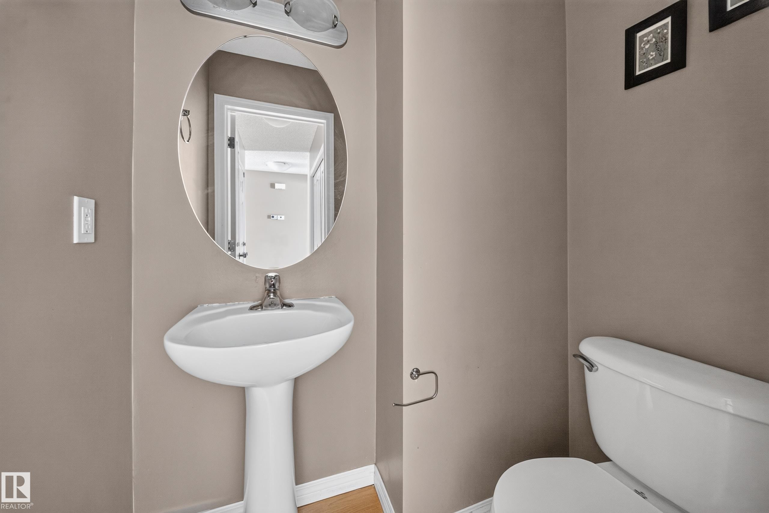 Pedestal sink with chrome faucet, an oval wall-mounted mirror, and a two-bulb vanity light fixture - 227 Cy Becker Blvd, Edmonton, AB