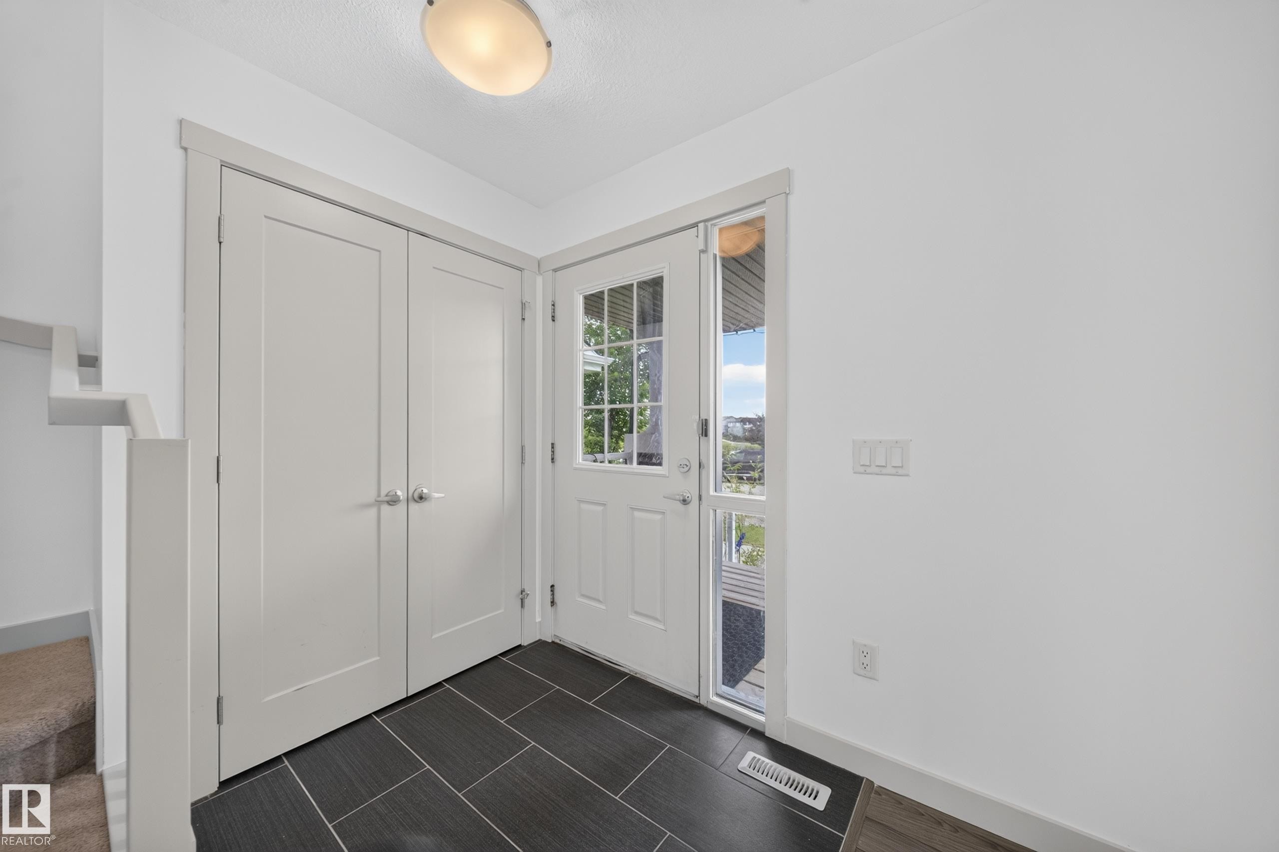 Entryway featuring dark rectangular floor tiles in a herringbone pattern, a white paneled door with a glass insert, and a sidelight - 227 Cy Becker Blvd, Edmonton, AB