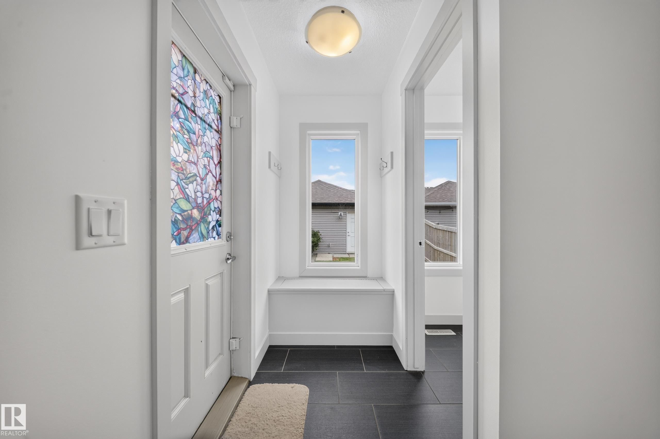 Entryway featuring a decorative glass door, black tile flooring, and a built-in window bench - 227 Cy Becker Blvd, Edmonton, AB