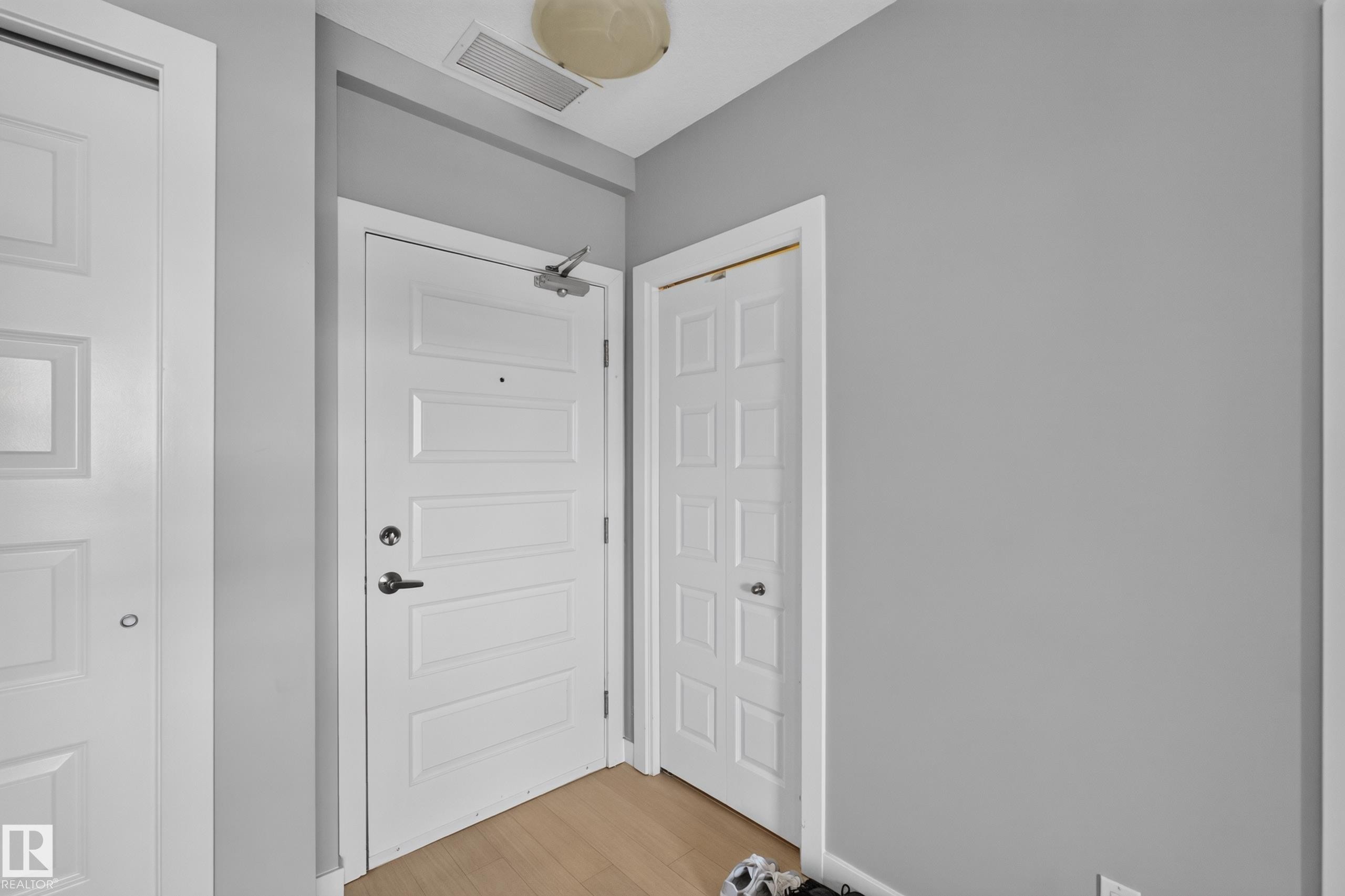 Entryway featuring light wood-finish flooring, white paneled doors, and painted walls - 706 5151 Windermere Boulevard, Edmonton, AB