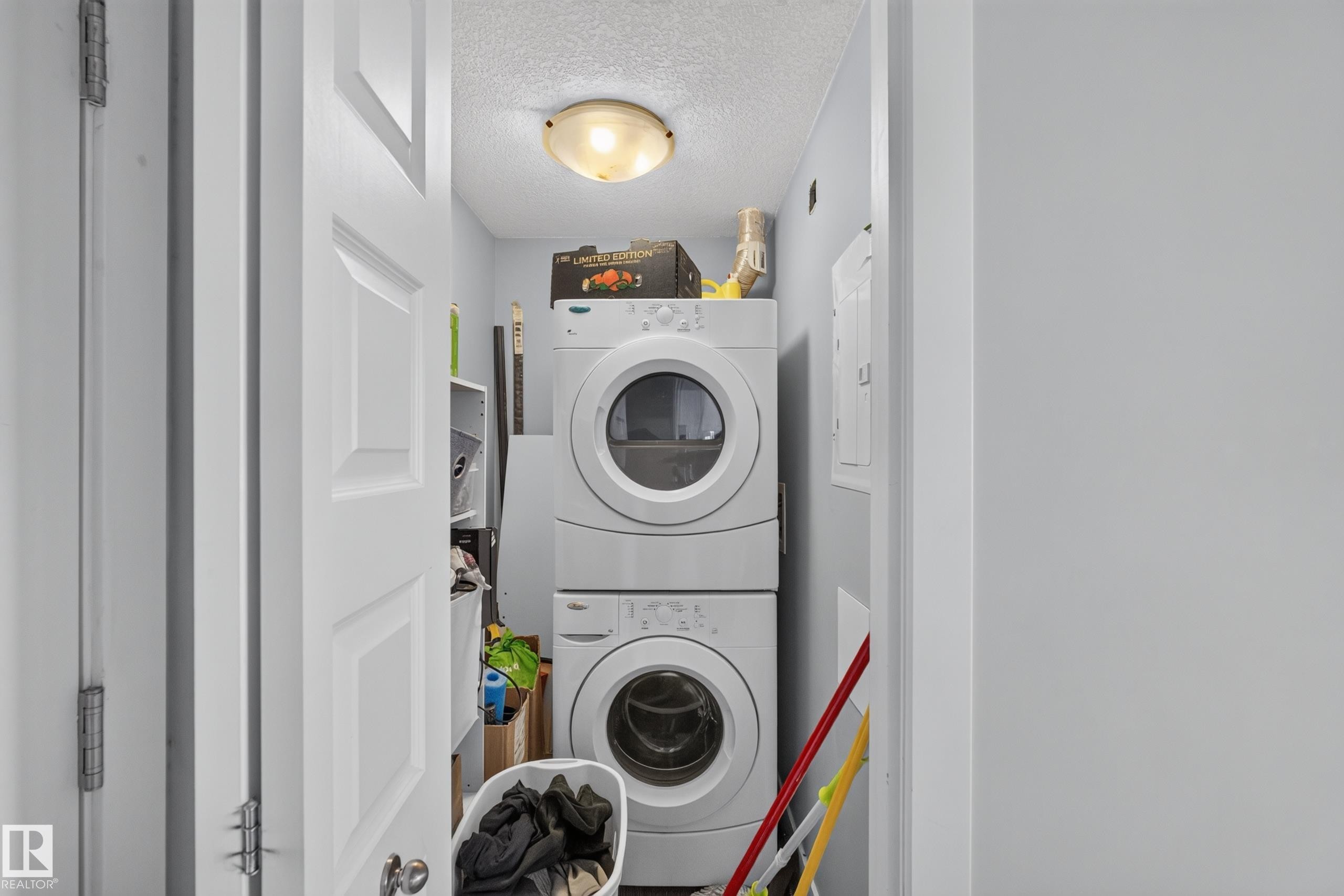 Dedicated laundry area featuring a stacked washer and dryer unit, overhead flush-mount lighting, and light blue wall paint - 706 5151 Windermere Boulevard, Edmonton, AB