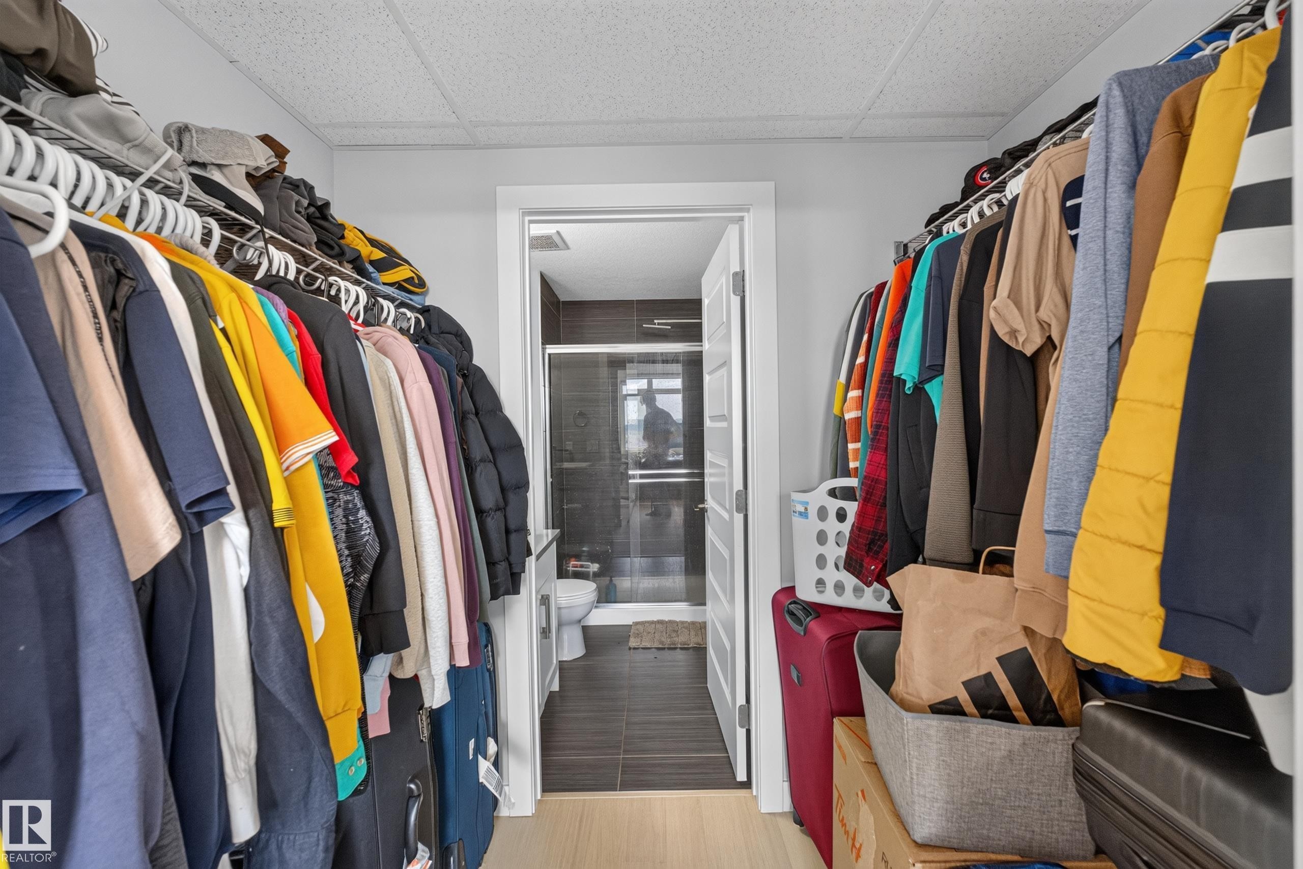 Walk-in closet featuring light wood-finish flooring, white wire shelving, and a doorway leading to a bathroom with dark tile flooring and a glass shower enclosure - 706 5151 Windermere Boulevard, Edmonton, AB