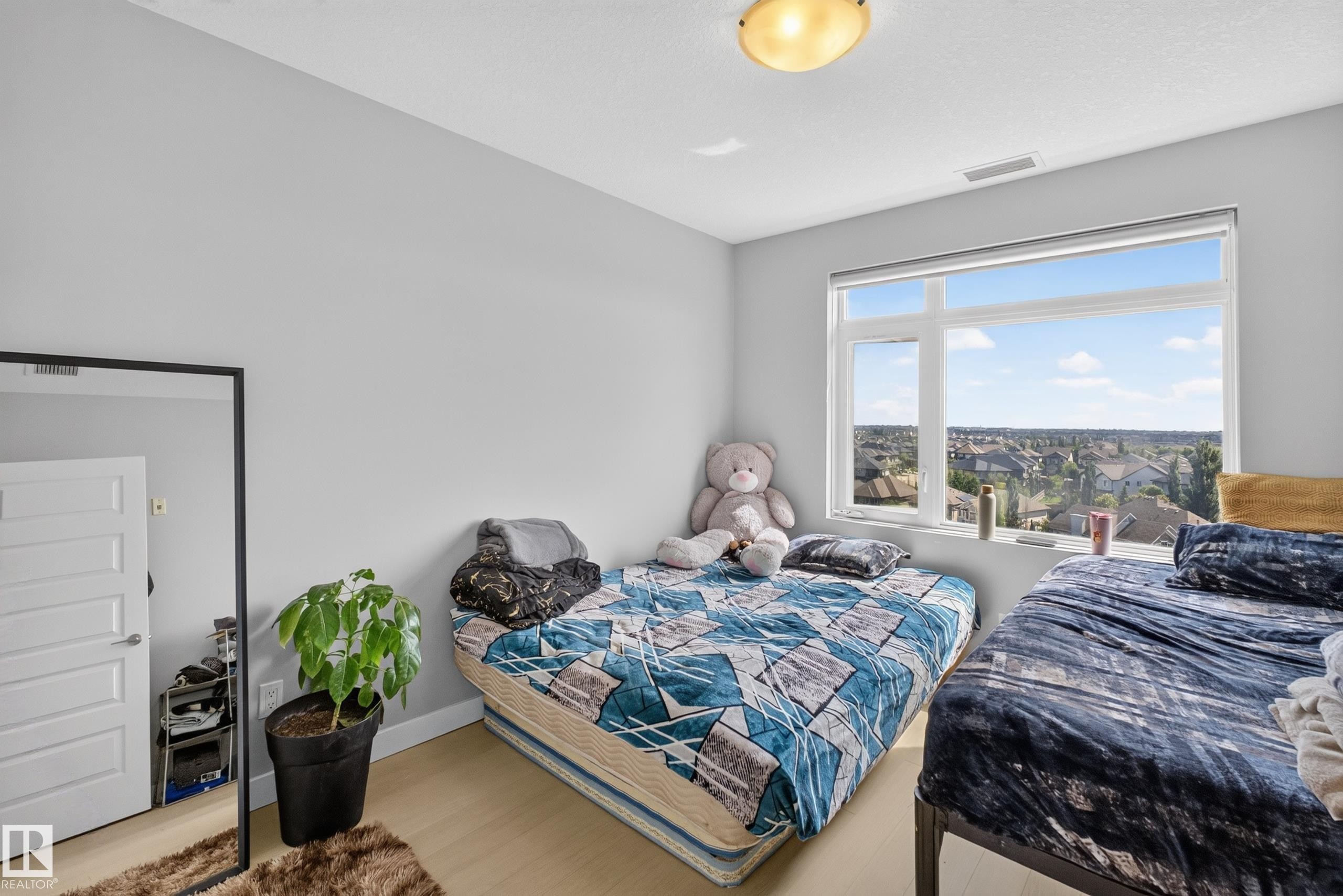Bright interior room featuring light-toned walls, wood-finish flooring, a large window, and an overhead flush-mount light fixture - 706 5151 Windermere Boulevard, Edmonton, AB