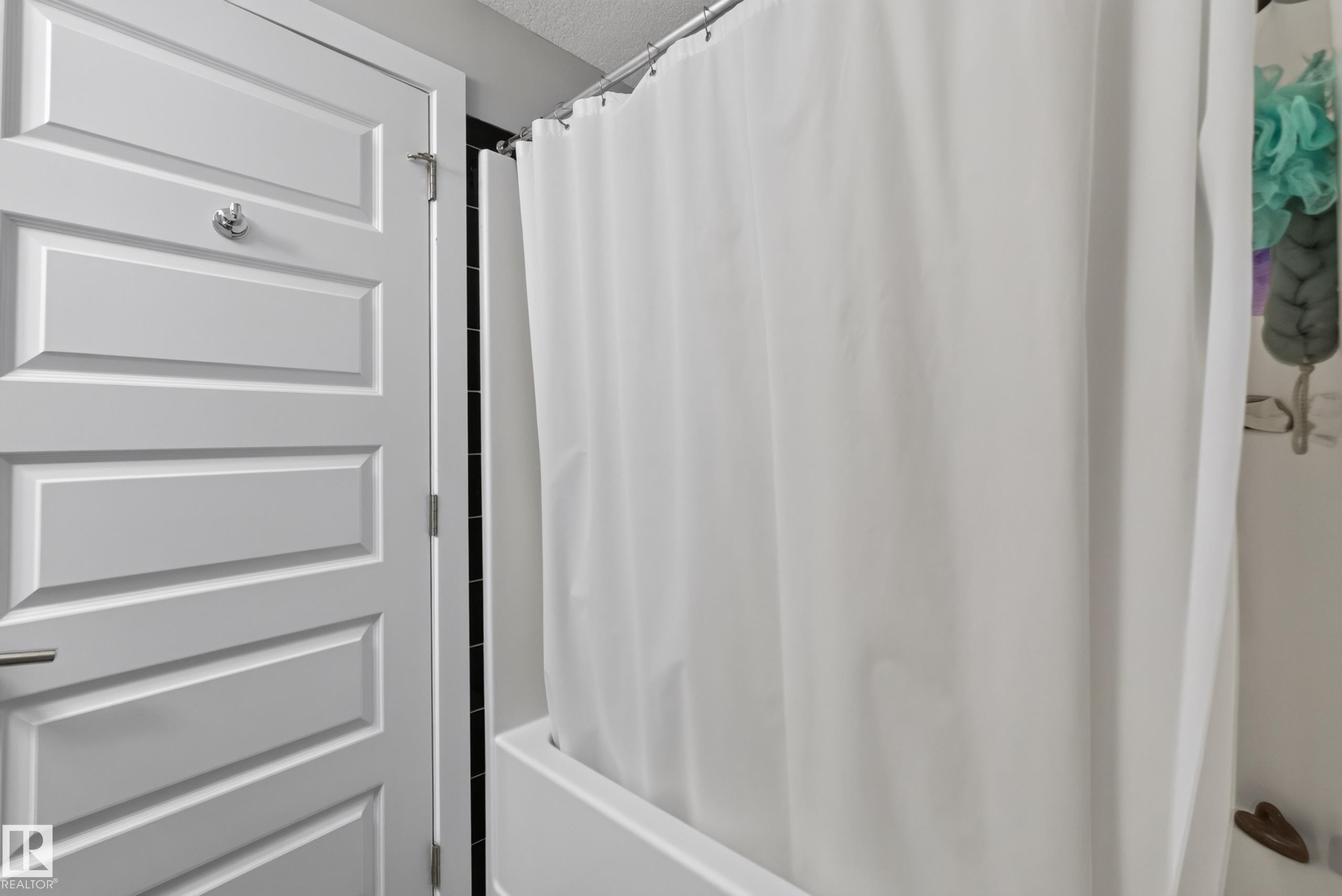 White paneled interior door with chrome hardware, featuring a full bathtub with a shower curtain - 706 5151 Windermere Boulevard, Edmonton, AB