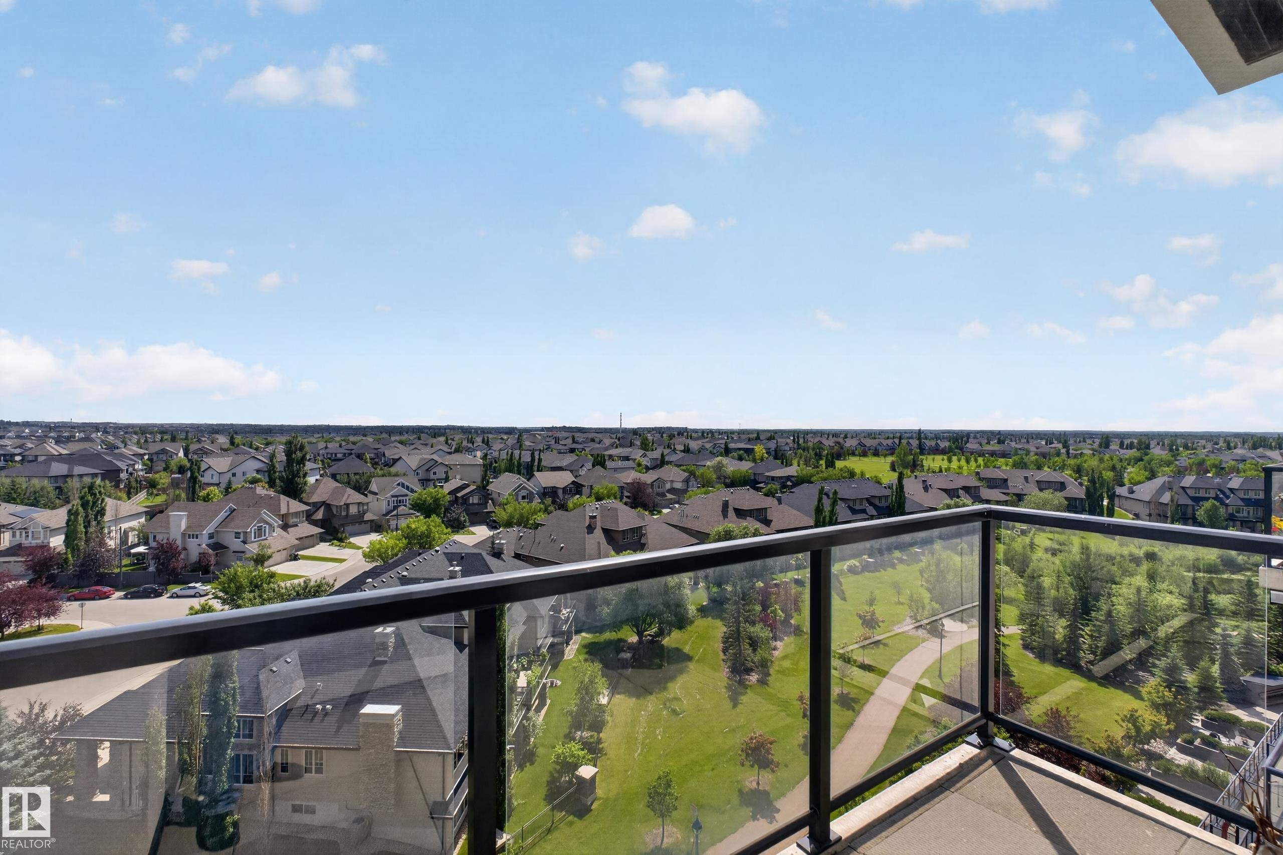 Balcony with glass railing overlooking a residential area with green spaces and walking paths - 706 5151 Windermere Boulevard, Edmonton, AB