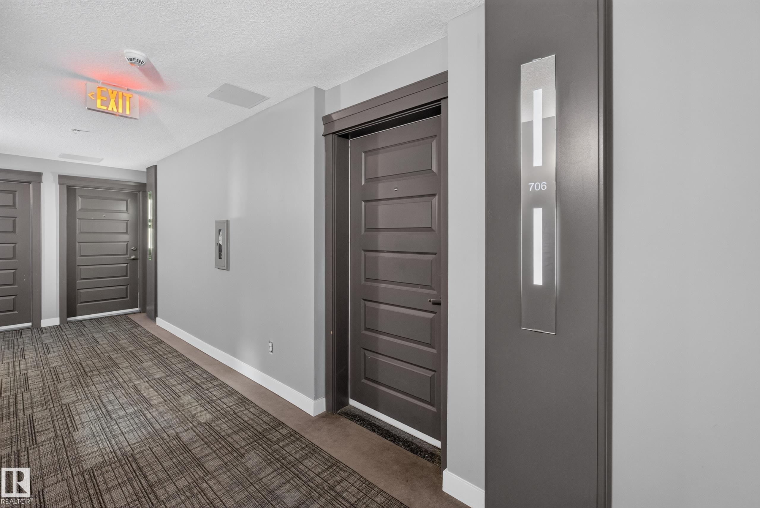 Corridor featuring light gray walls, dark wood-finish doors, and patterned carpet flooring - 706 5151 Windermere Boulevard, Edmonton, AB
