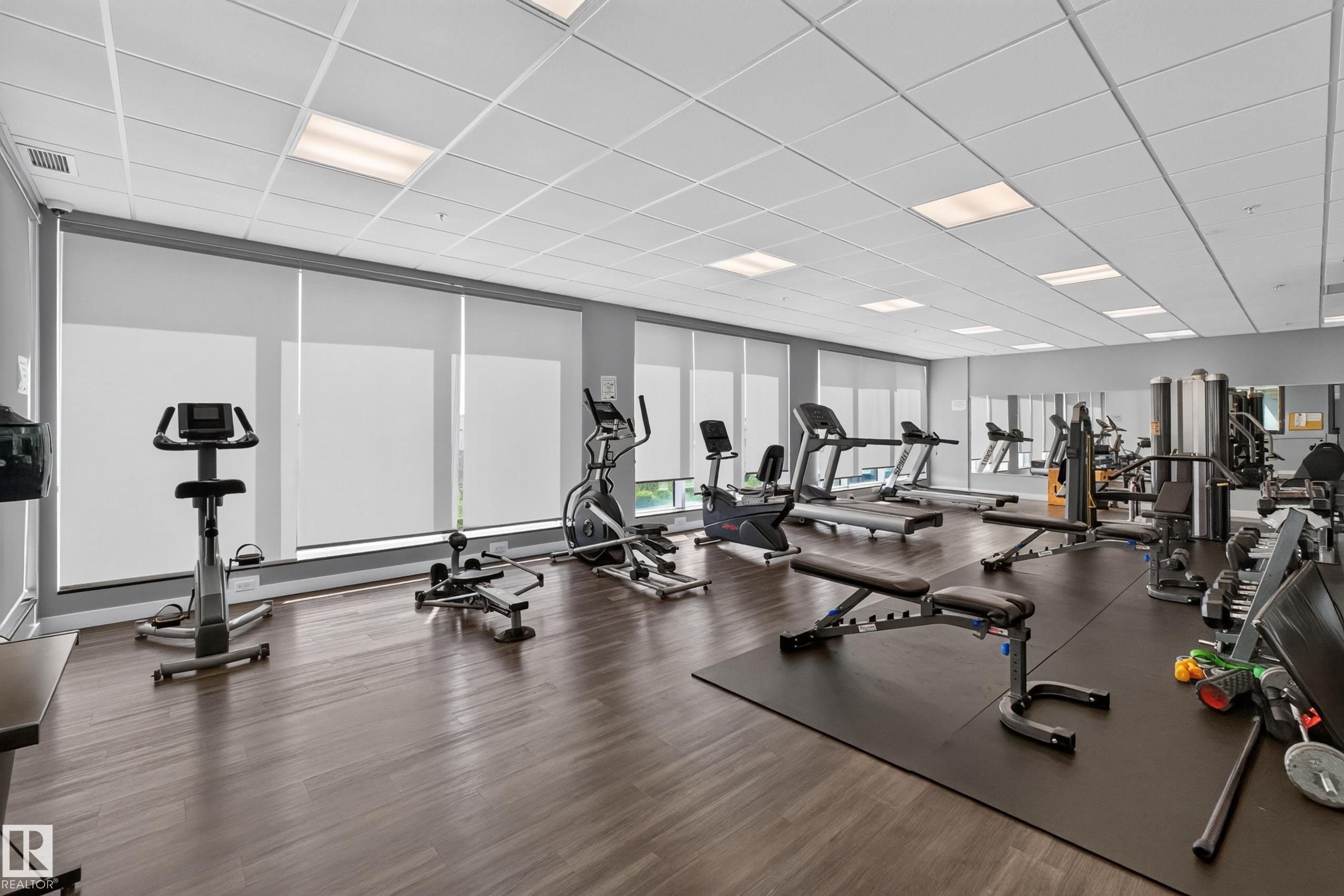 Fitness center with wood-finish flooring, ample natural light from multiple windows, and extensive mirrored walls - 706 5151 Windermere Boulevard, Edmonton, AB
