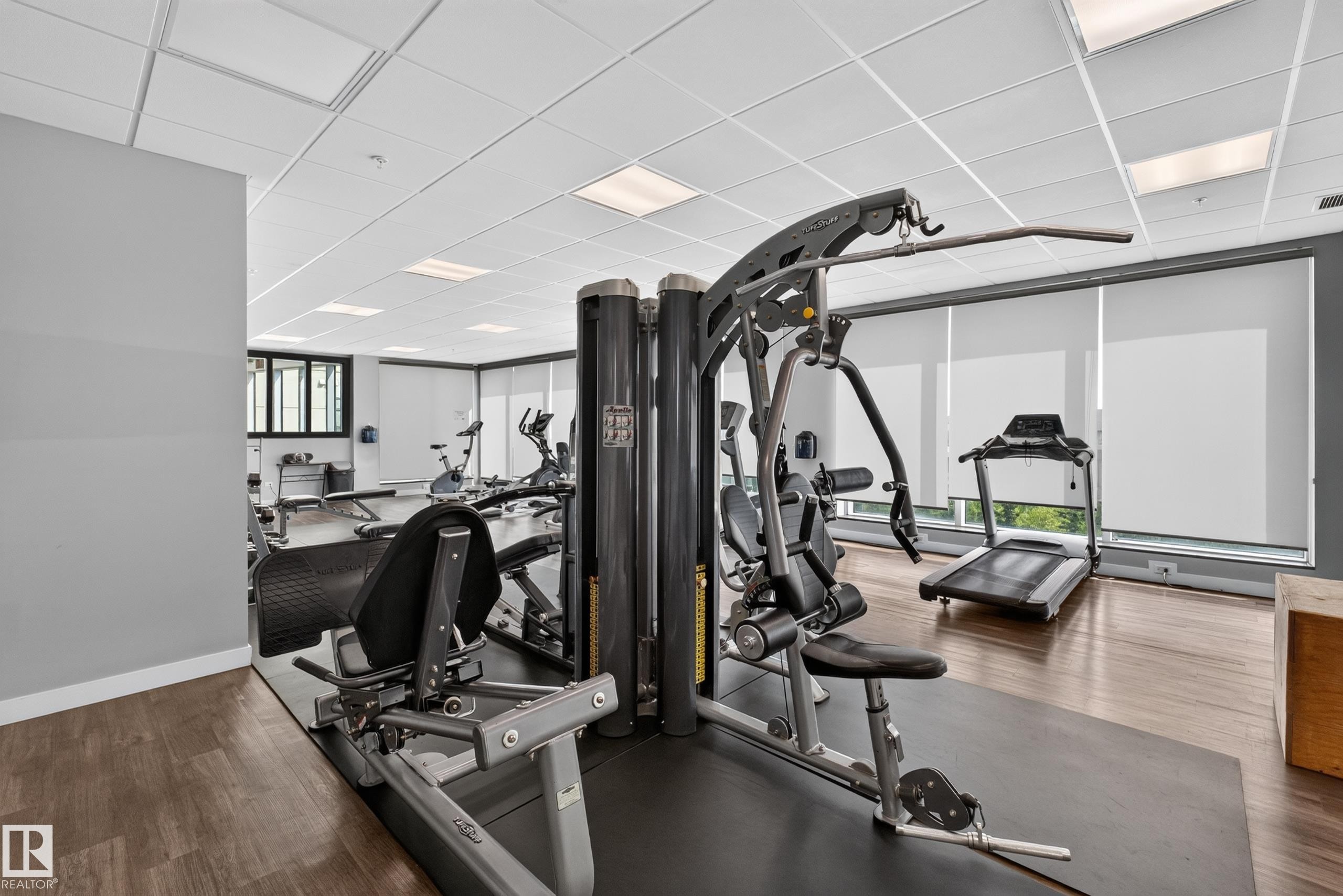 Fitness center with wood-finish flooring, drop ceiling with integrated lighting, and multiple exercise machines - 706 5151 Windermere Boulevard, Edmonton, AB