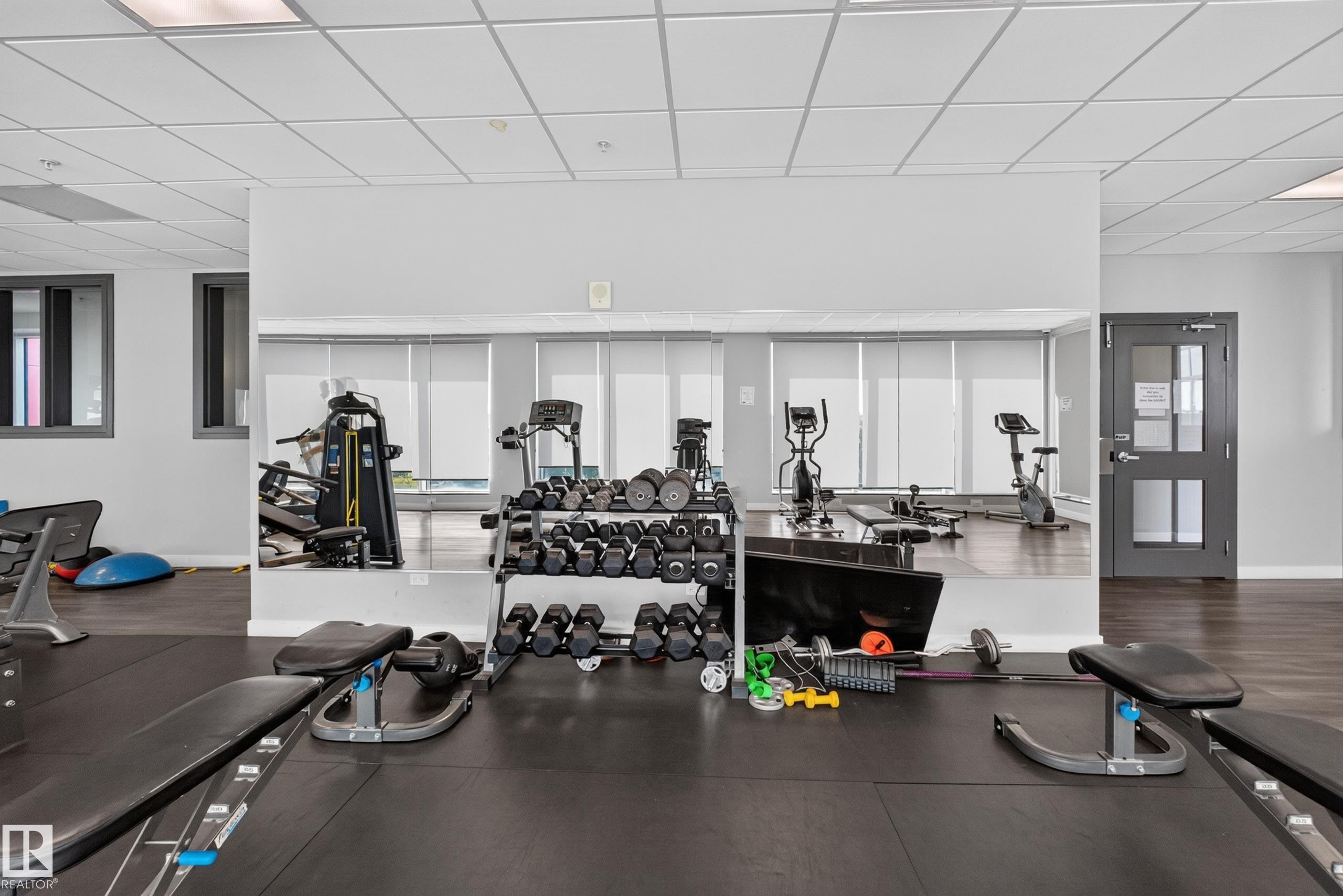 Fitness center featuring a mirrored wall, rubber flooring, and track lighting - 706 5151 Windermere Boulevard, Edmonton, AB