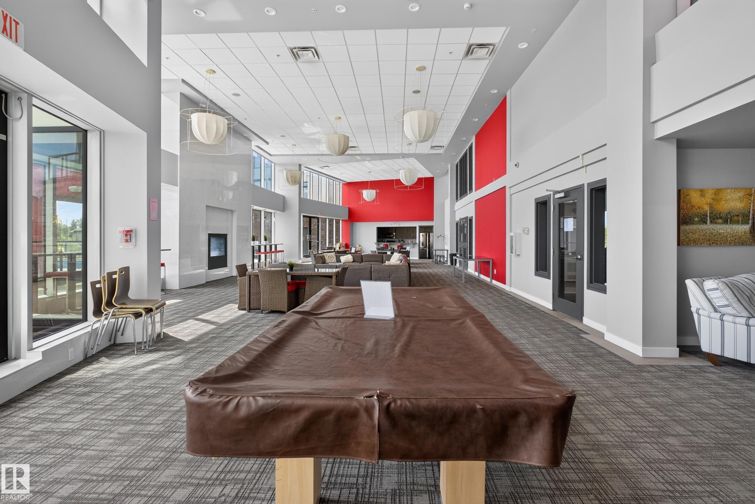 Spacious common area featuring high ceilings, contemporary pendant lighting, extensive window lines, a built-in fireplace, and patterned carpet flooring - 706 5151 Windermere Boulevard, Edmonton, AB