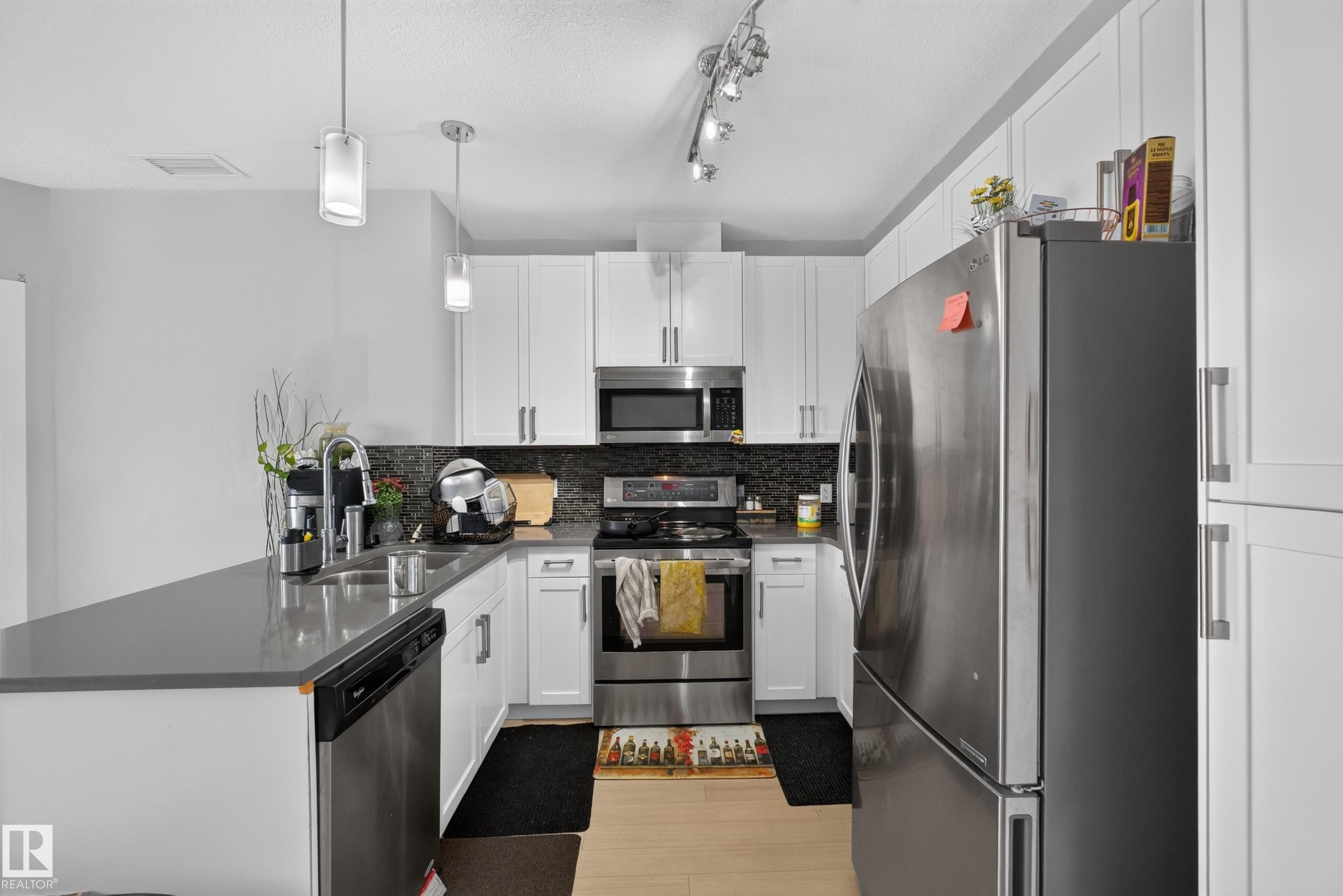 Modern kitchen featuring white shaker cabinetry, stainless steel appliances, dark stone-finish countertops, and a mosaic tile backsplash - 706 5151 Windermere Boulevard, Edmonton, AB