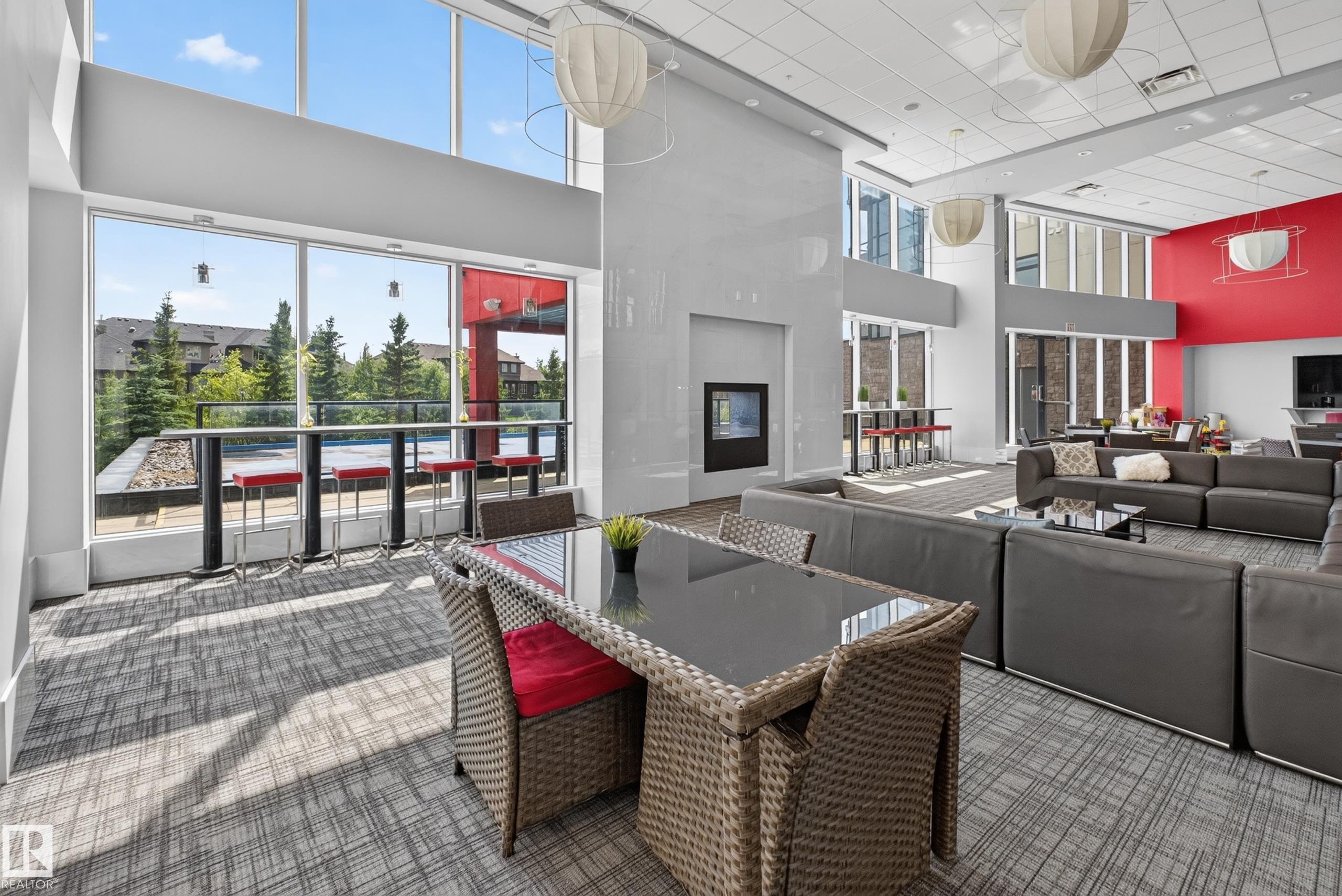 Spacious common area featuring floor-to-ceiling windows, high ceilings, a built-in electric fireplace, and contemporary light fixtures - 706 5151 Windermere Boulevard, Edmonton, AB