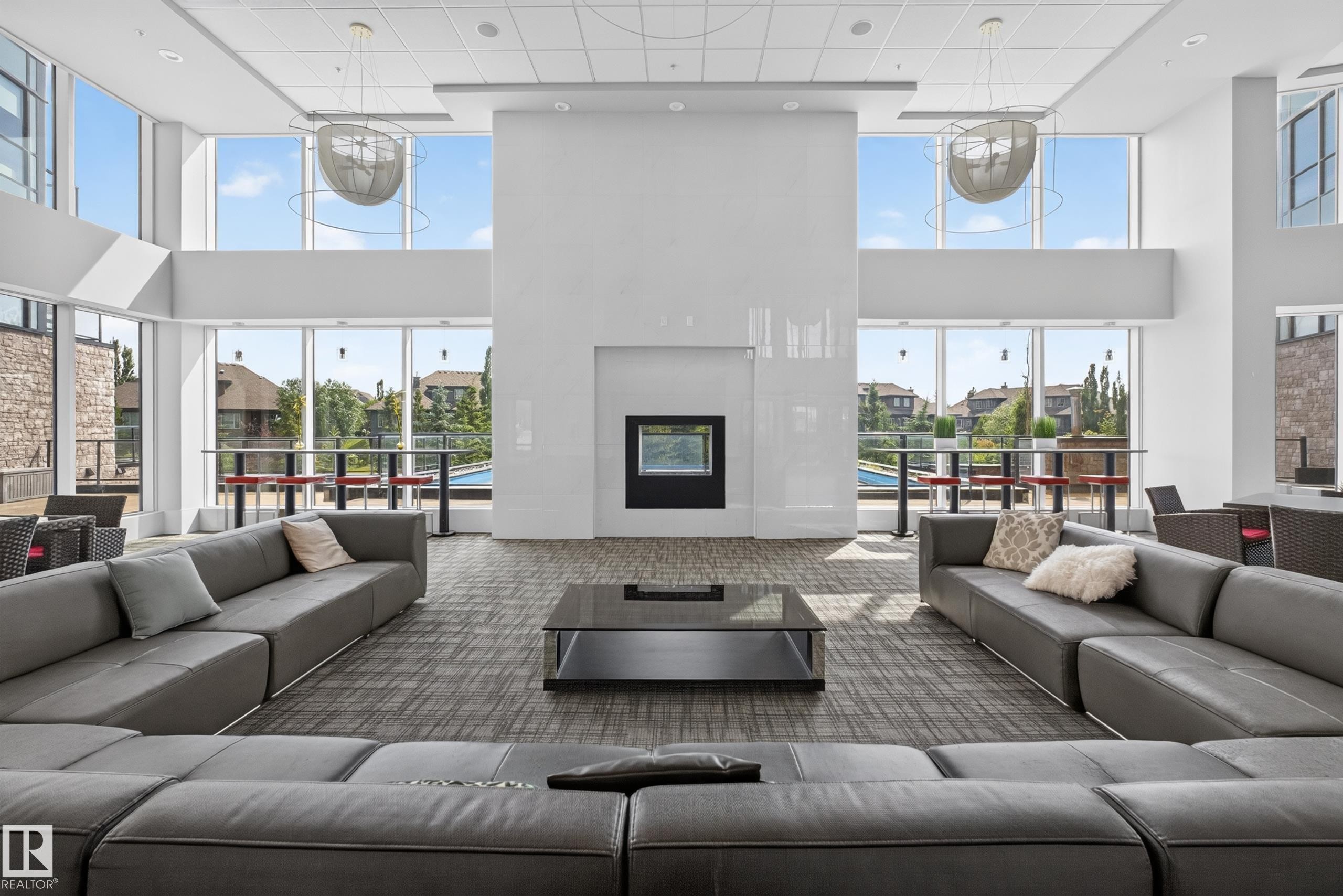 Spacious communal room featuring a floor-to-ceiling window wall, a central fireplace, recessed lighting, and modern pendant light fixtures - 706 5151 Windermere Boulevard, Edmonton, AB