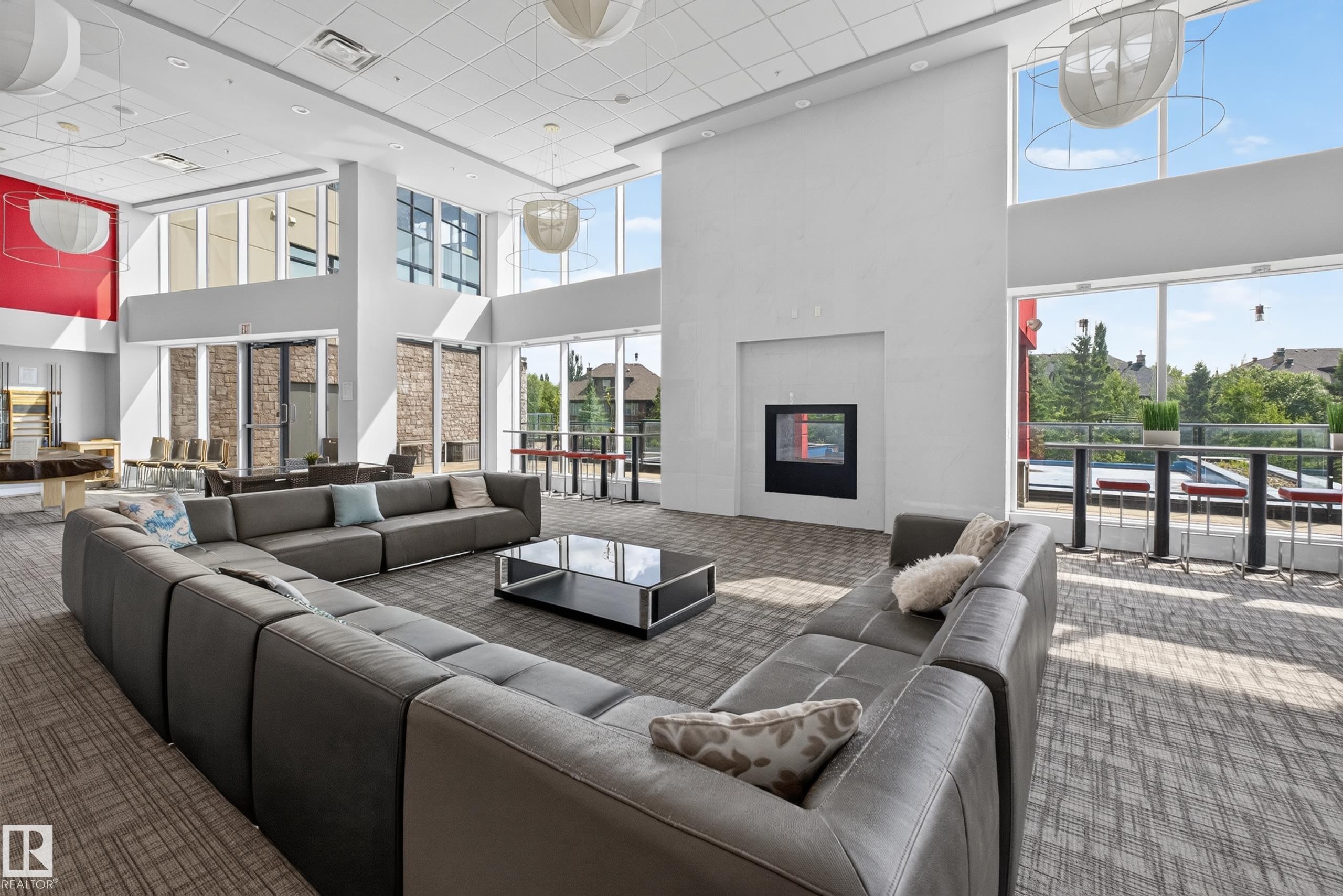 Spacious common area featuring an integrated fireplace, high ceilings, full-height windows, and contemporary pendant lighting - 706 5151 Windermere Boulevard, Edmonton, AB