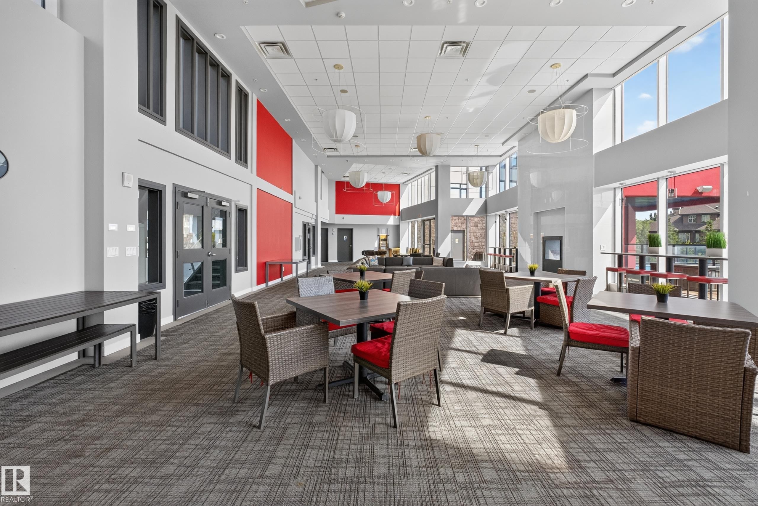 Spacious communal area featuring high ceilings, extensive window walls, and contemporary pendant lighting - 706 5151 Windermere Boulevard, Edmonton, AB