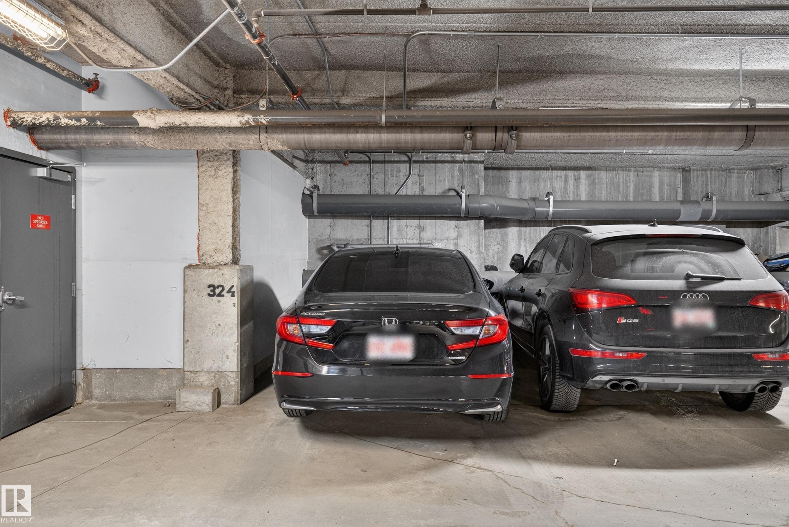 Concrete parking garage with exposed ceiling pipes and concrete support pillars - 706 5151 Windermere Boulevard, Edmonton, AB