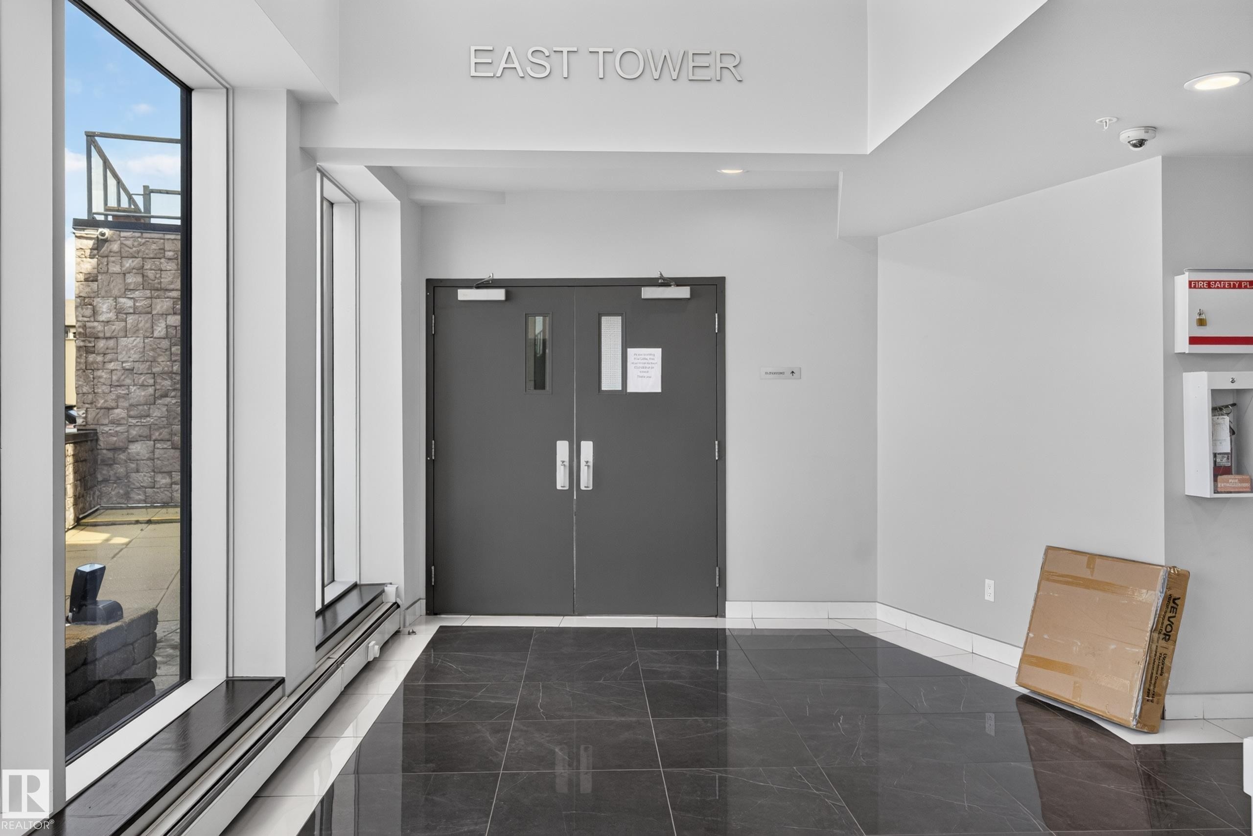 Lobby entrance featuring large format dark tile flooring, white walls, and floor-to-ceiling windows - 706 5151 Windermere Boulevard, Edmonton, AB