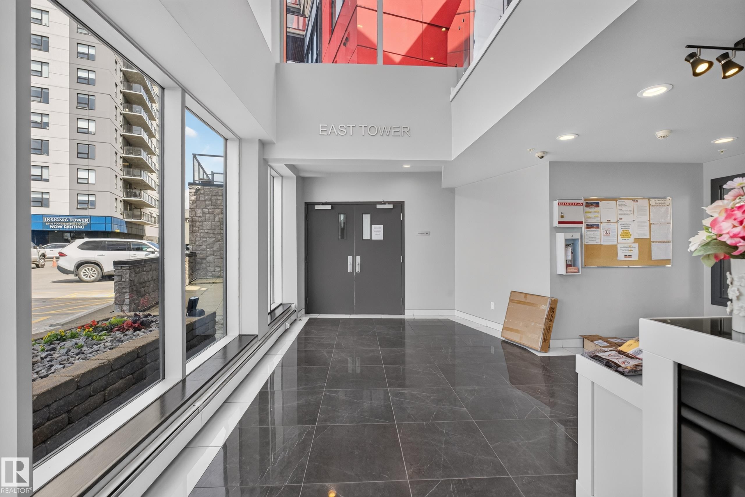 Spacious lobby featuring polished dark tile flooring, a high ceiling, and full-height windows - 706 5151 Windermere Boulevard, Edmonton, AB