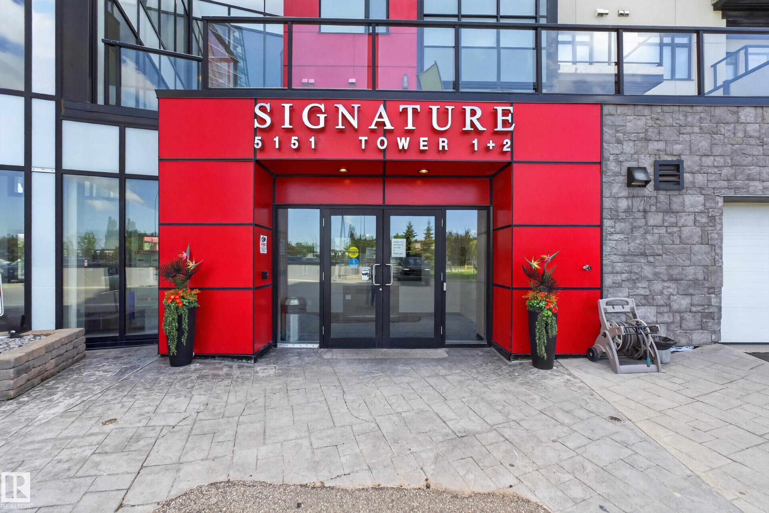 Modern building entrance featuring vibrant red paneling and a "SIGNATURE" sign - 706 5151 Windermere Boulevard, Edmonton, AB