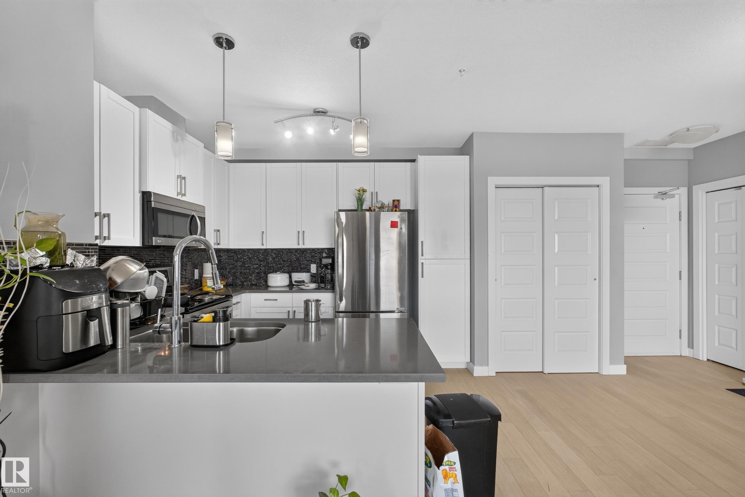 Modern kitchen featuring white cabinetry, dark countertops, stainless steel appliances, and a dark mosaic tile backsplash - 706 5151 Windermere Boulevard, Edmonton, AB