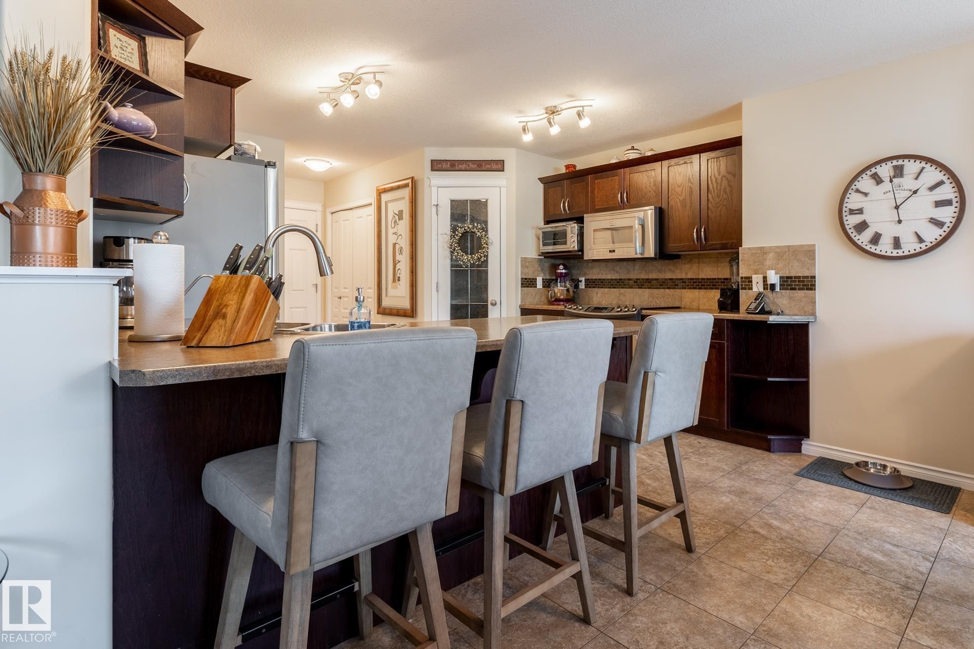 Kitchen with dark wood cabinetry, stainless steel appliances, and a tiled backsplash - 5820 7 Avenue Sw, Edmonton, AB - Indoor