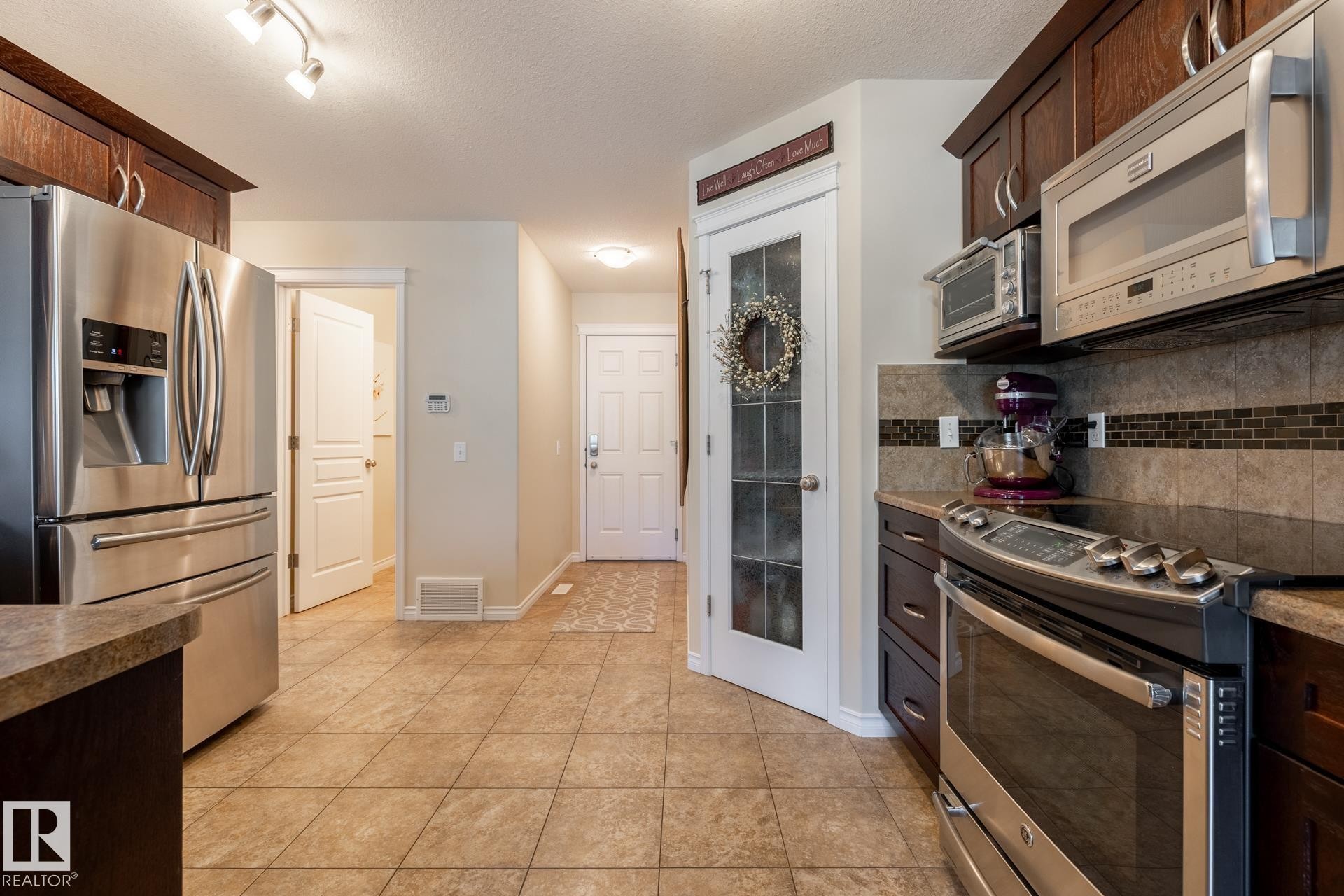 Kitchen featuring stainless steel appliances, dark wood-finish cabinetry, tile flooring, and a patterned tile backsplash - 5820 7 Avenue Sw, Edmonton, AB - Indoor Photo Showing Kitchen