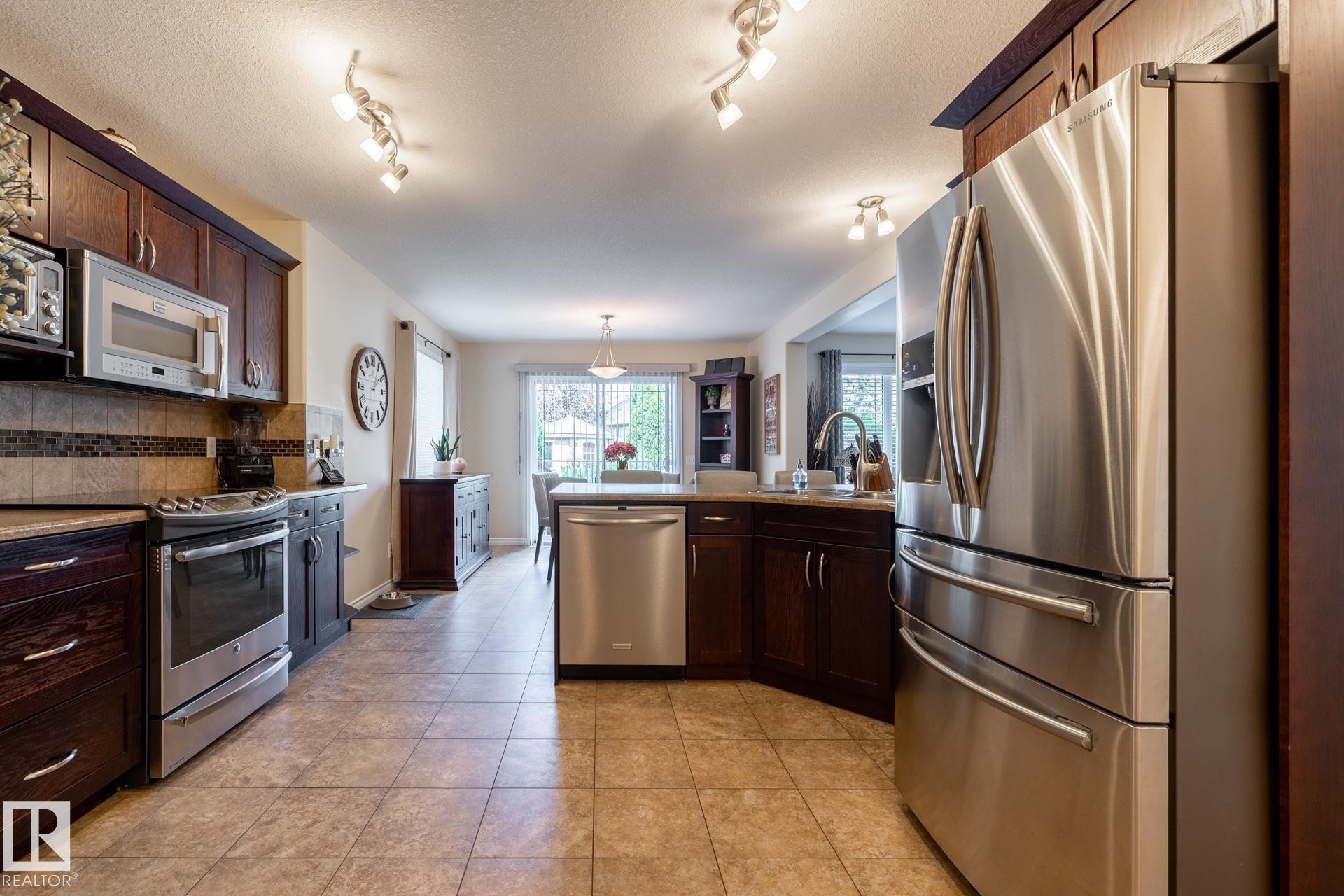 Kitchen featuring stainless steel appliances, dark wood-finish cabinetry, tile flooring, and track lighting - 5820 7 Avenue Sw, Edmonton, AB - Indoor Photo Showing Kitchen