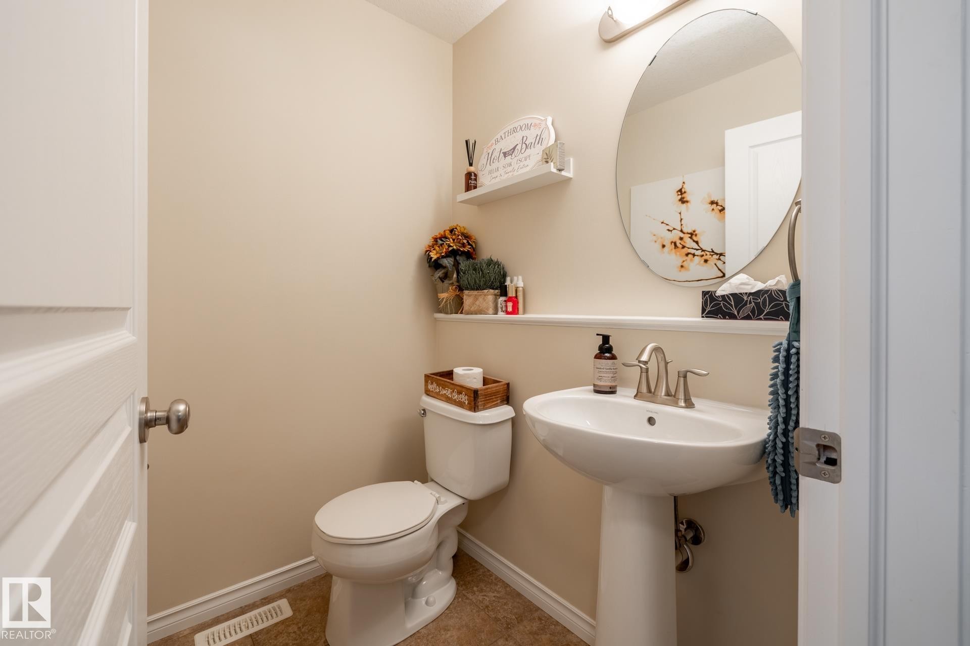 Pedestal sink with brushed nickel faucet, an oval mirror, and tile flooring - 5820 7 Avenue Sw, Edmonton, AB - Indoor Photo Showing Bathroom