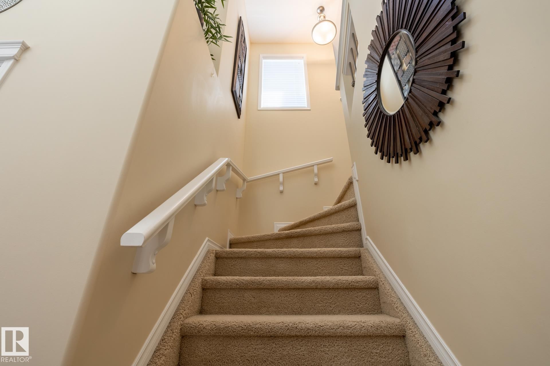 Carpeted stairway featuring a white handrail, light beige wall paint, and natural light from an upper-level window - 5820 7 Avenue Sw, Edmonton, AB - Indoor Photo Showing Other Room