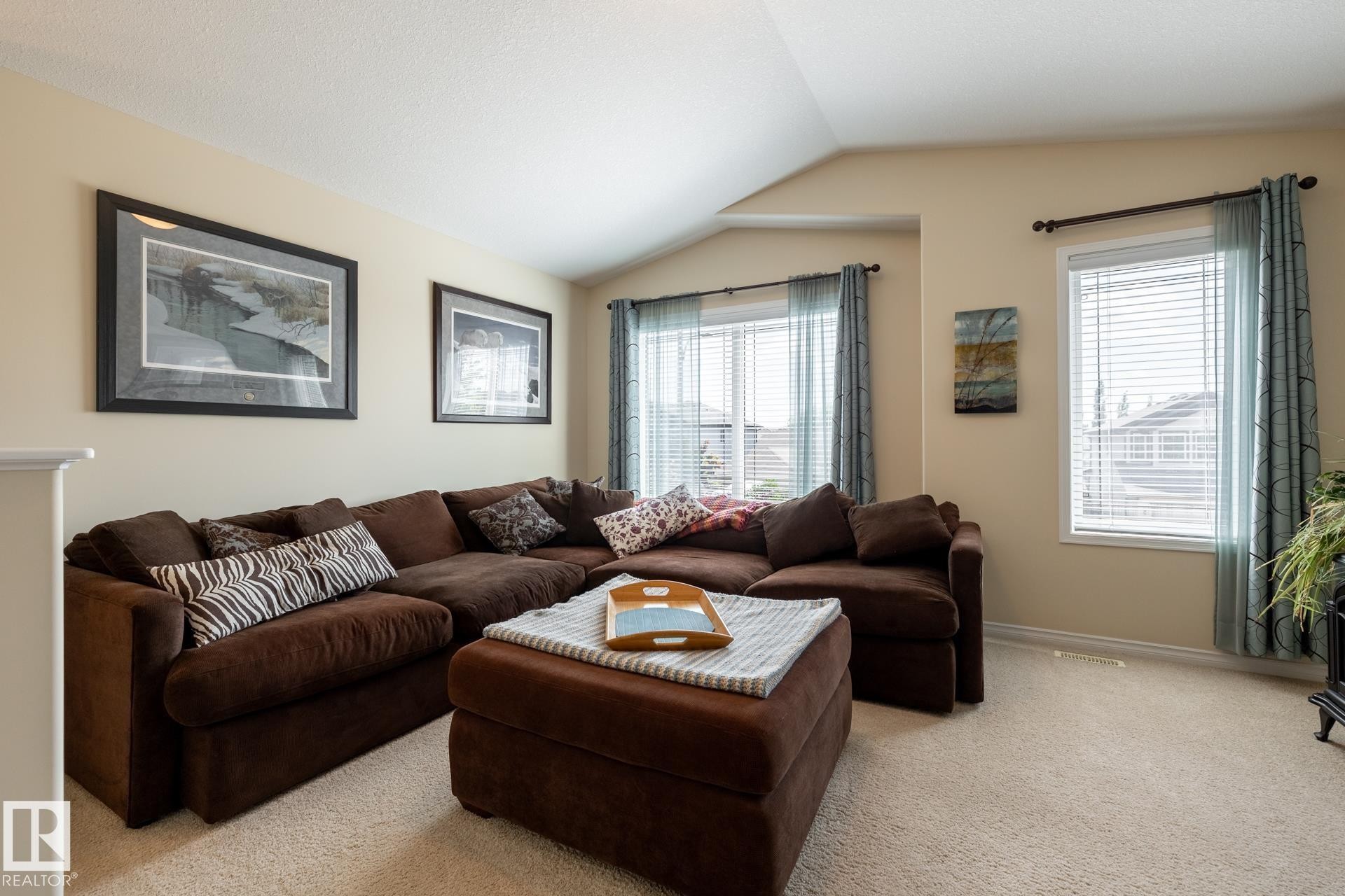 Carpeted living area featuring vaulted ceilings, light neutral wall paint, and multiple windows with blinds and drapery - 5820 7 Avenue Sw, Edmonton, AB - Indoor Photo Showing Living Room