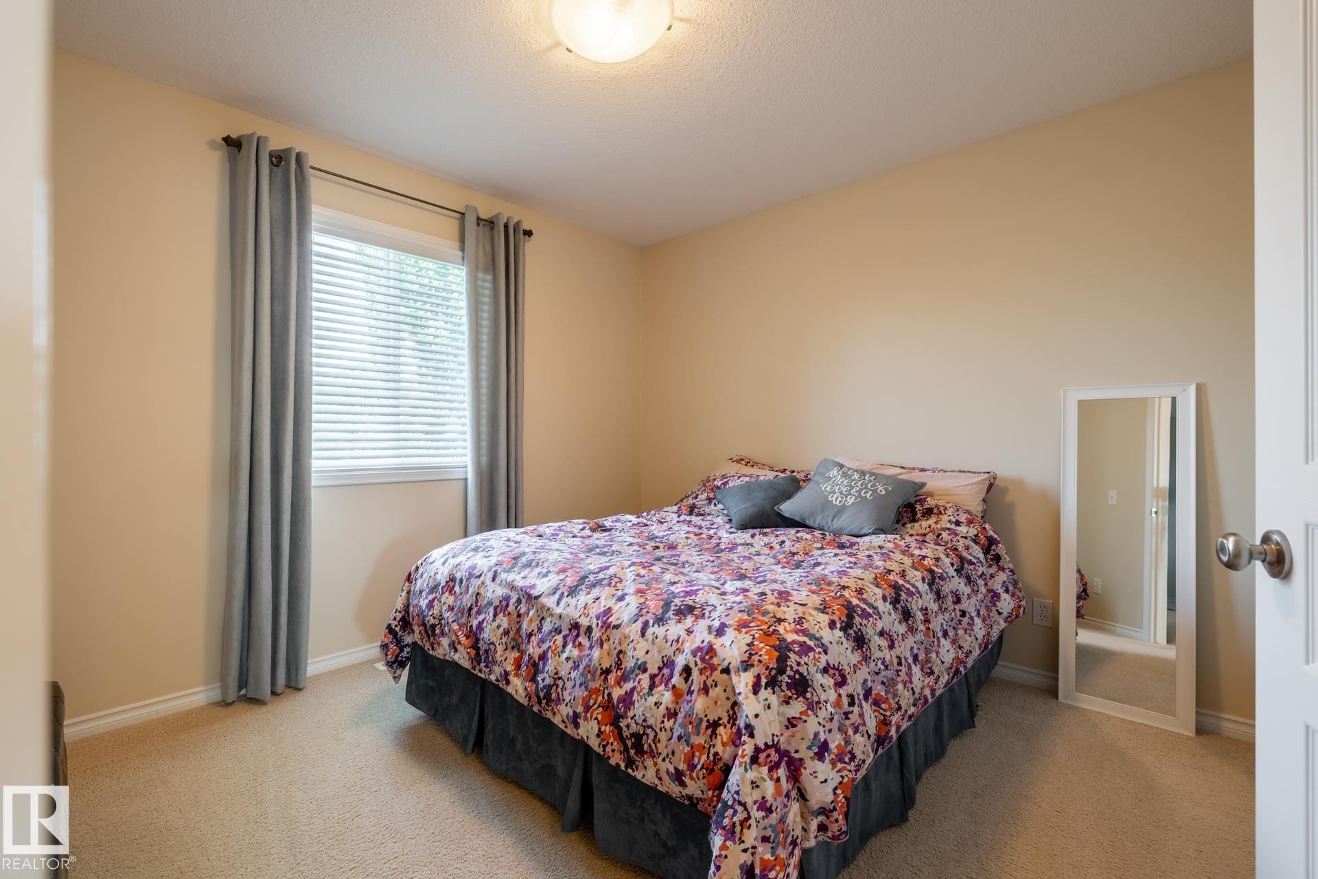 Carpeted room featuring a window with blinds and drapes, light beige walls, and a white ceiling - 5820 7 Avenue Sw, Edmonton, AB - Indoor Photo Showing Bedroom